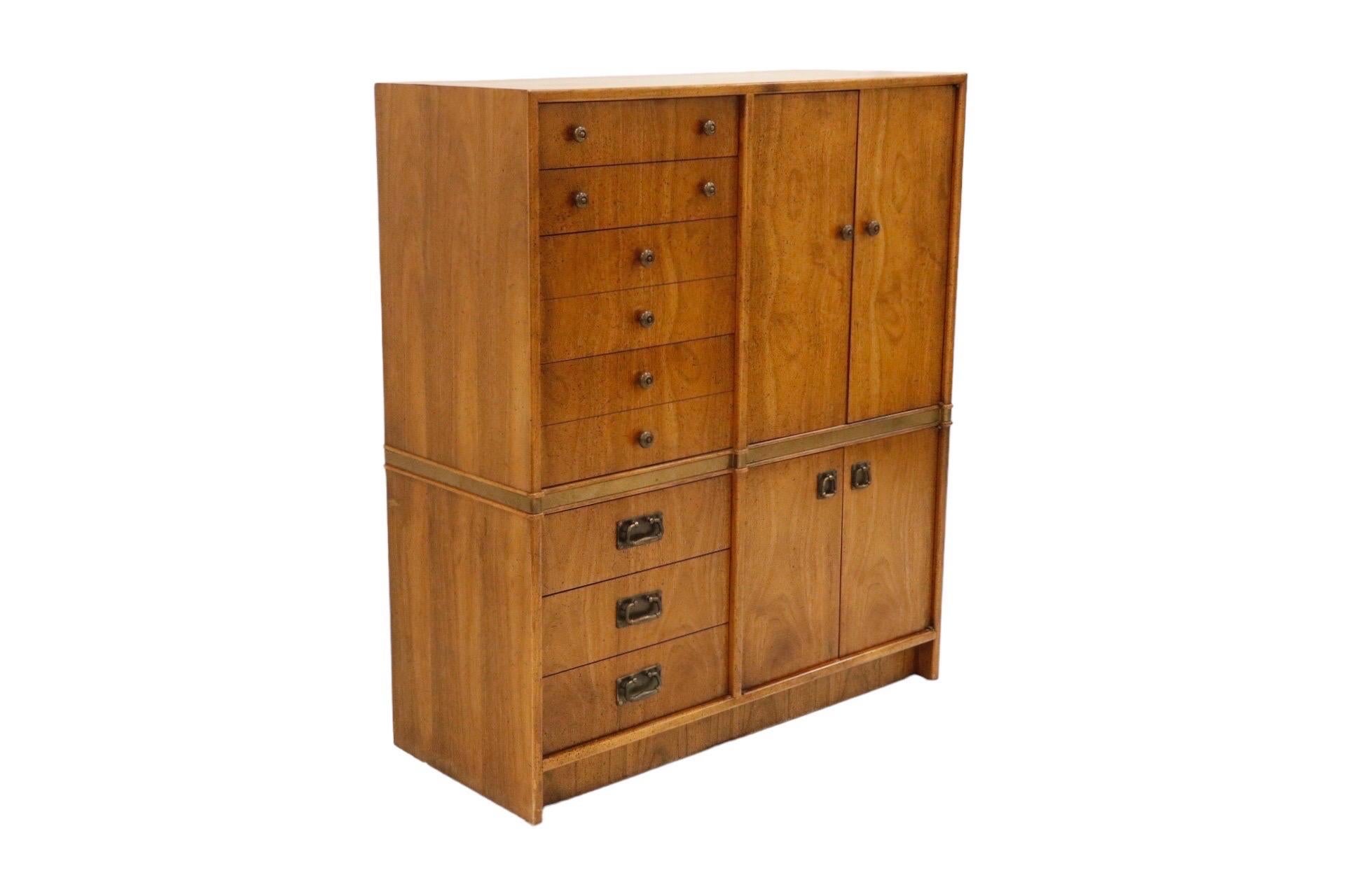 A 1972 campaign style gentleman’s dresser or chiffonier made by Hickory Manufacturing Company, decorated with Paldao veneers. Four graduated drawers to the left, and an upper cabinet to the right, are separated from three lower drawers and a lower