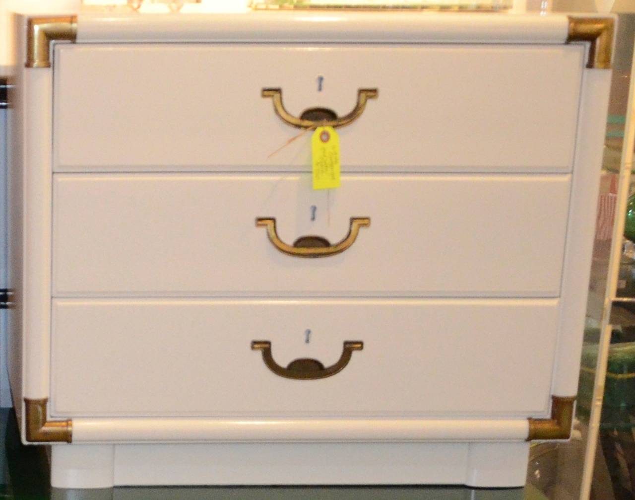 Offered is a Mid-Century Modern Campaign style lacquered in white with brass accents bedside table / chest of drawers. This chest of drawers / bedside table / stand would look fabulous in a child's or teenager's bedroom. This piece could be