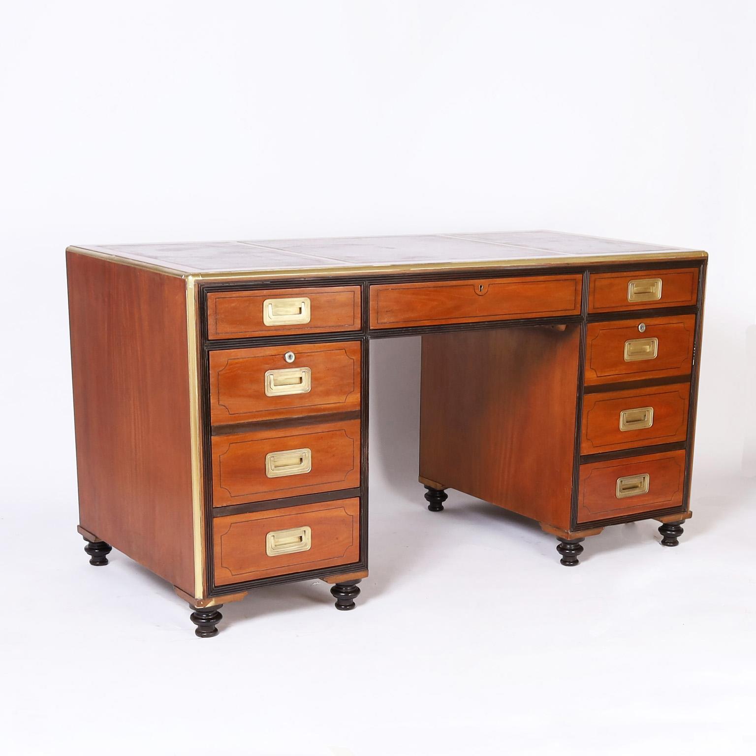 With a perfect blend of modern and traditional this mahogany nine drawer desk has three tooled brown leather panels on top, a two toned case with ebonized trim, brass campaign hardware, open shelves on the back and turned feet. Signed Baker