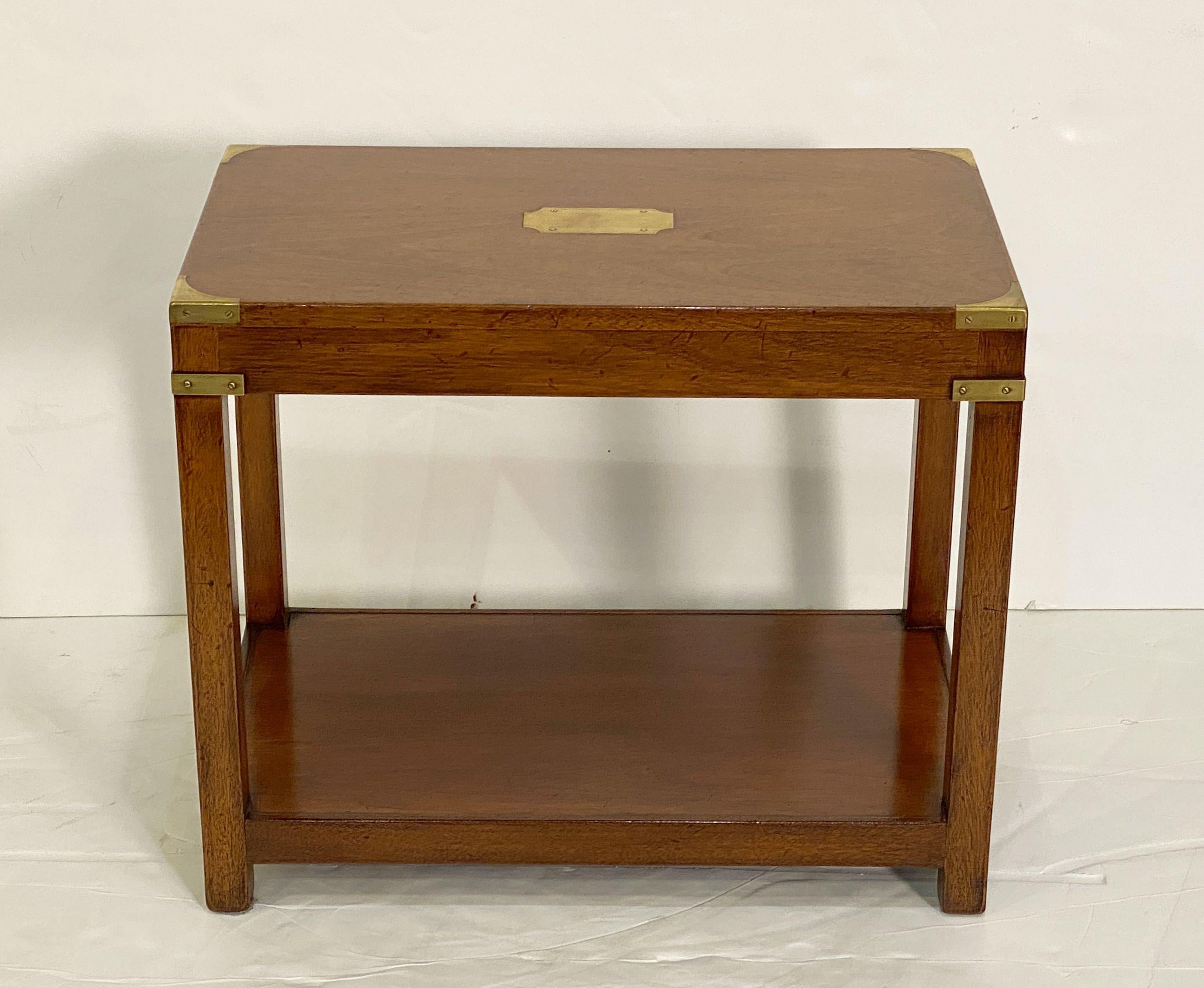 A fine British Campaign style two-tiered rectangular side or end table of patinated teak featuring hand-cut brass accents on the corners and a brass cartouche in the top center.

Perfect for use as a cocktail (low) or coffee table.