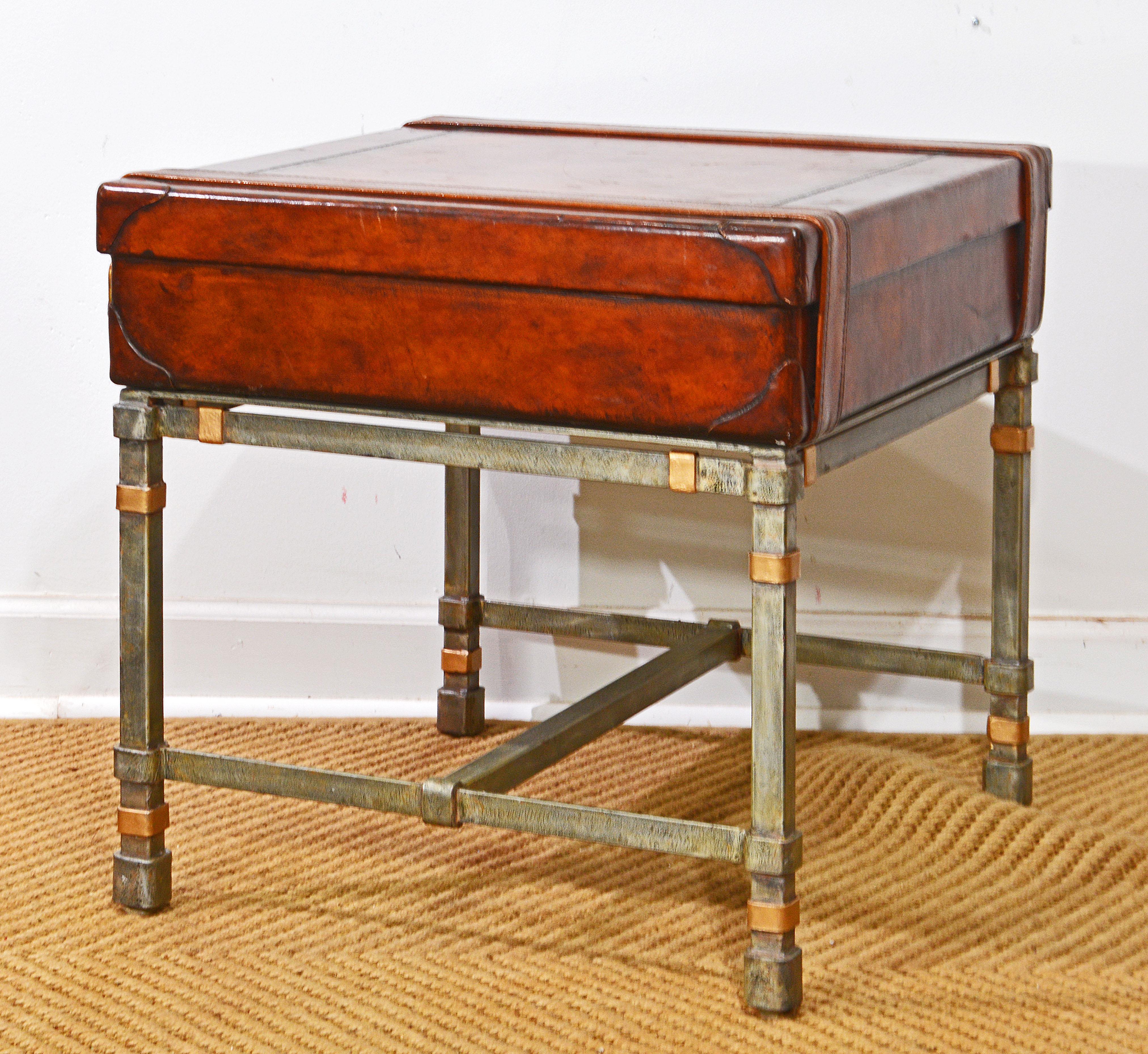 Unique likely British Colonial Leather luggage table on a hand forged antiique metal finish stand with intentionalle sligtly worn gold finish accents. The table consists of a used old world leather suitcase with drawer resting on a hand forged