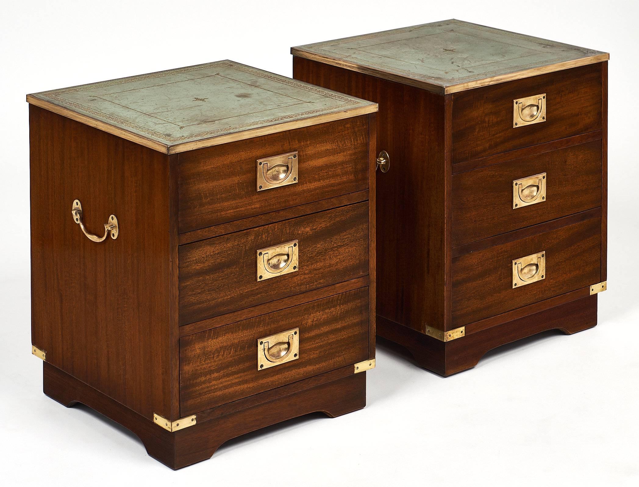 A fine vintage pair of English campaign chests made of mahogany and finished with a French polish for luster. They have green leather tops embossed with gold leafing. All of the brass trims and hardware are original. Each has three dovetailed