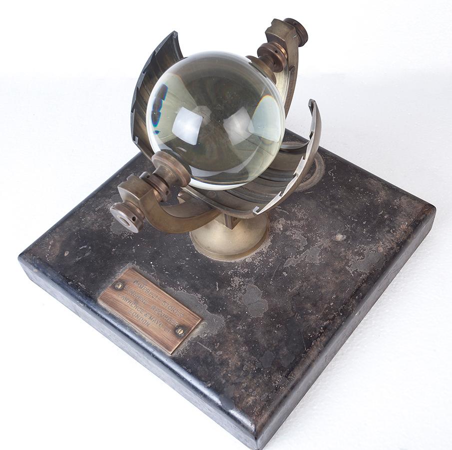 A Campbell Stokes sunshine recorder from the early 1900s made by Lawrence and Mayo, Ltd., and documented as such. The device consists of a solid glass sphere, 4 inches in diameter, that concentrates the sun's rays to an intense spot on a calibrated