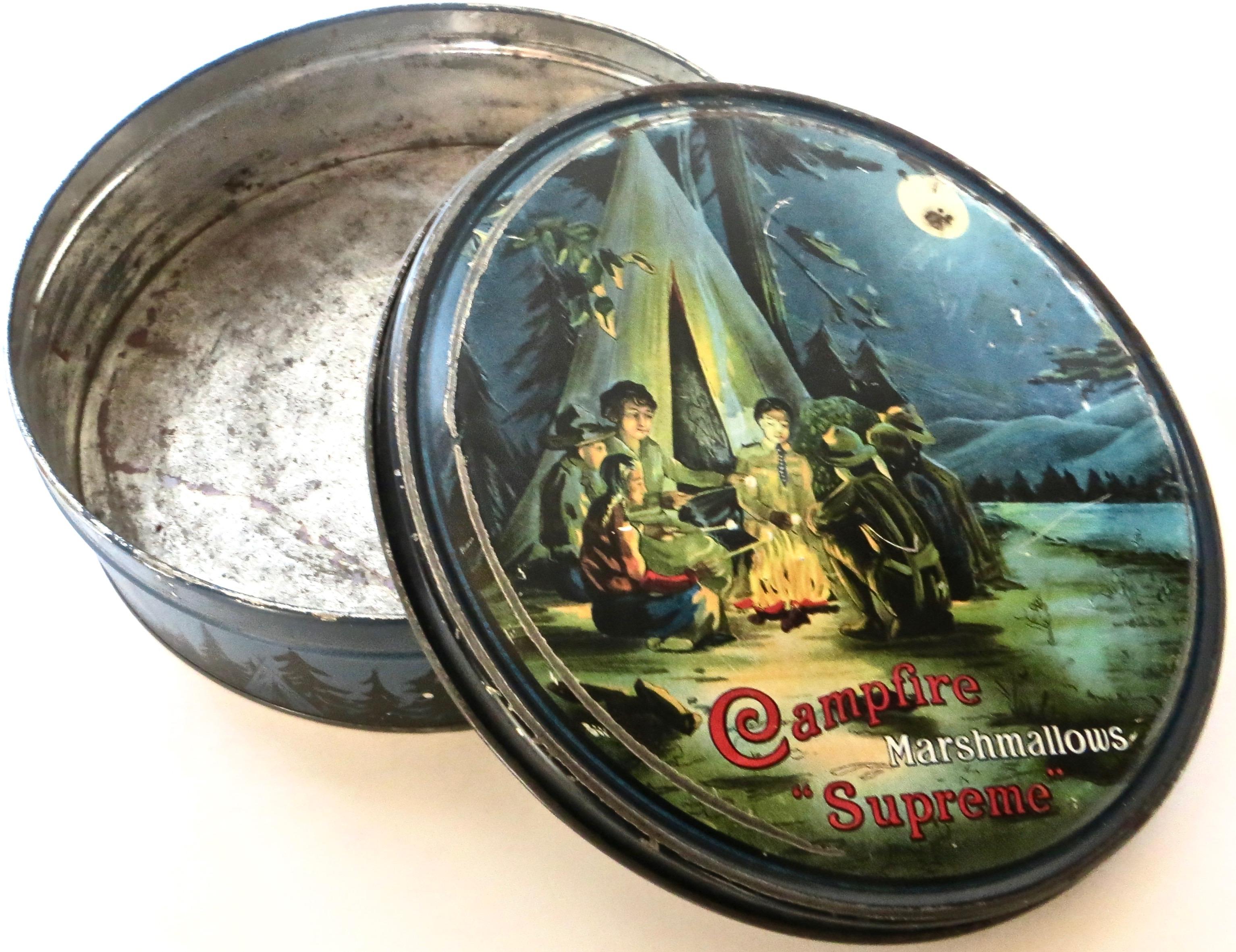 This is a rare tin that was used to sell and promote marshmallows. The top of the tin is decorated to reflect the Boy Scouts in their ubiquitous camping tradition of sitting around the campfire, roasting marshmallows on a brightly lit full moon