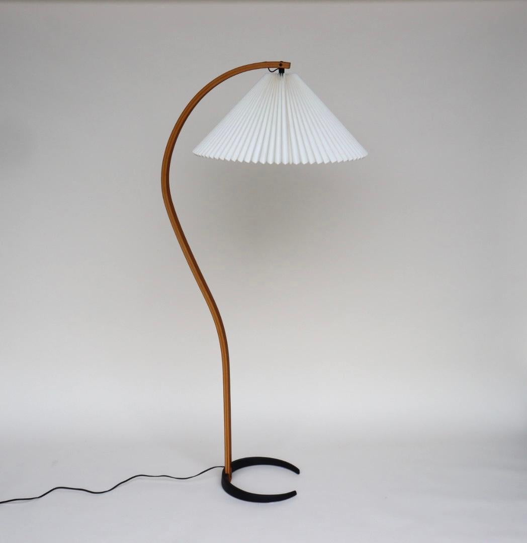 This is a Caprani floor lamp, designed by Danish manufacturer Mads Caprani AS, circa 1960s. This vintage lamp features a sculptural bent plywood stand with an elegant curve, a cast iron crescent shaped base, and original pleated linen shade. The