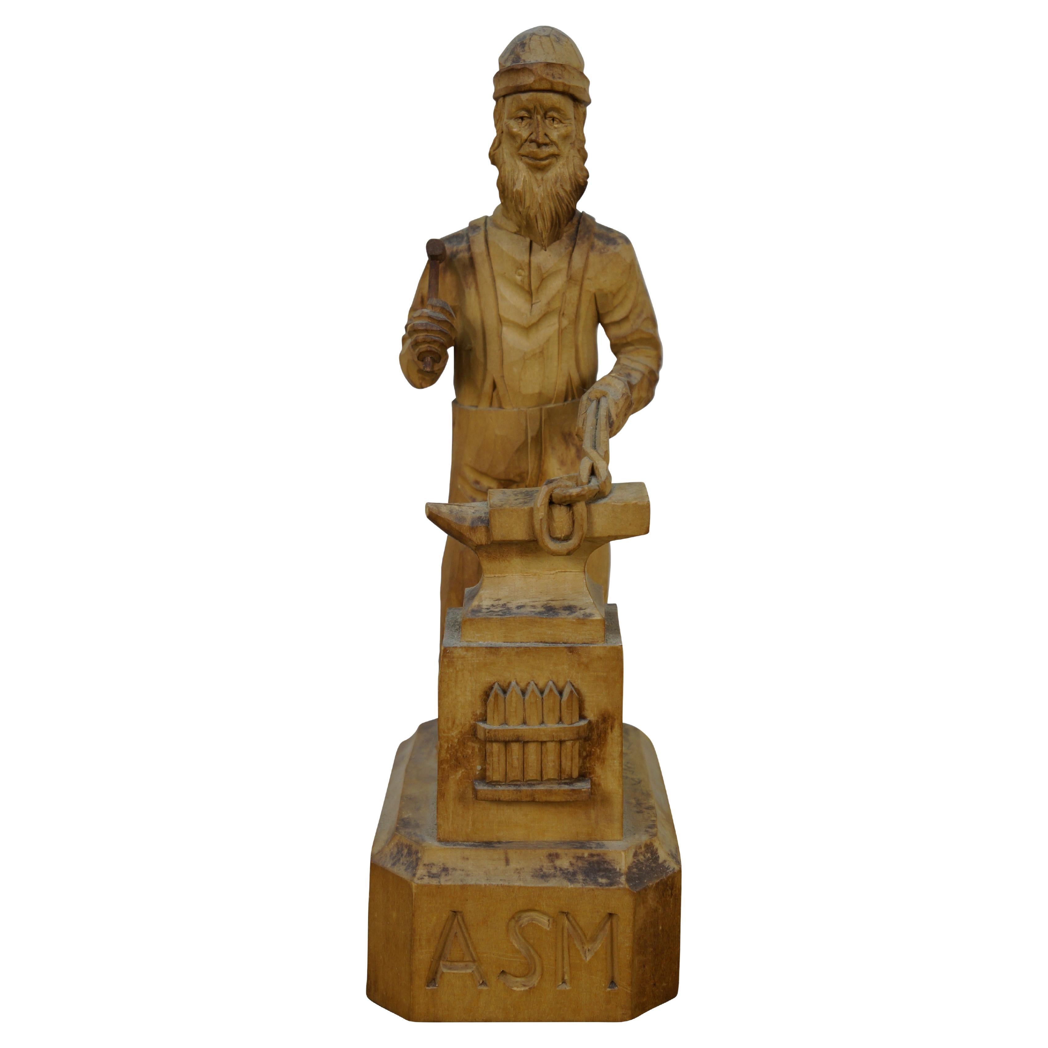 Vers le milieu du XXe siècle, sculpture / figurine en bois sculptée à la main par Simon Dube.  La sculpture représente un forgeron/ferronnier qui forge une chaîne sur son enclume. Les initiales ASM sont gravées sur le devant. Signé sur le dessus du