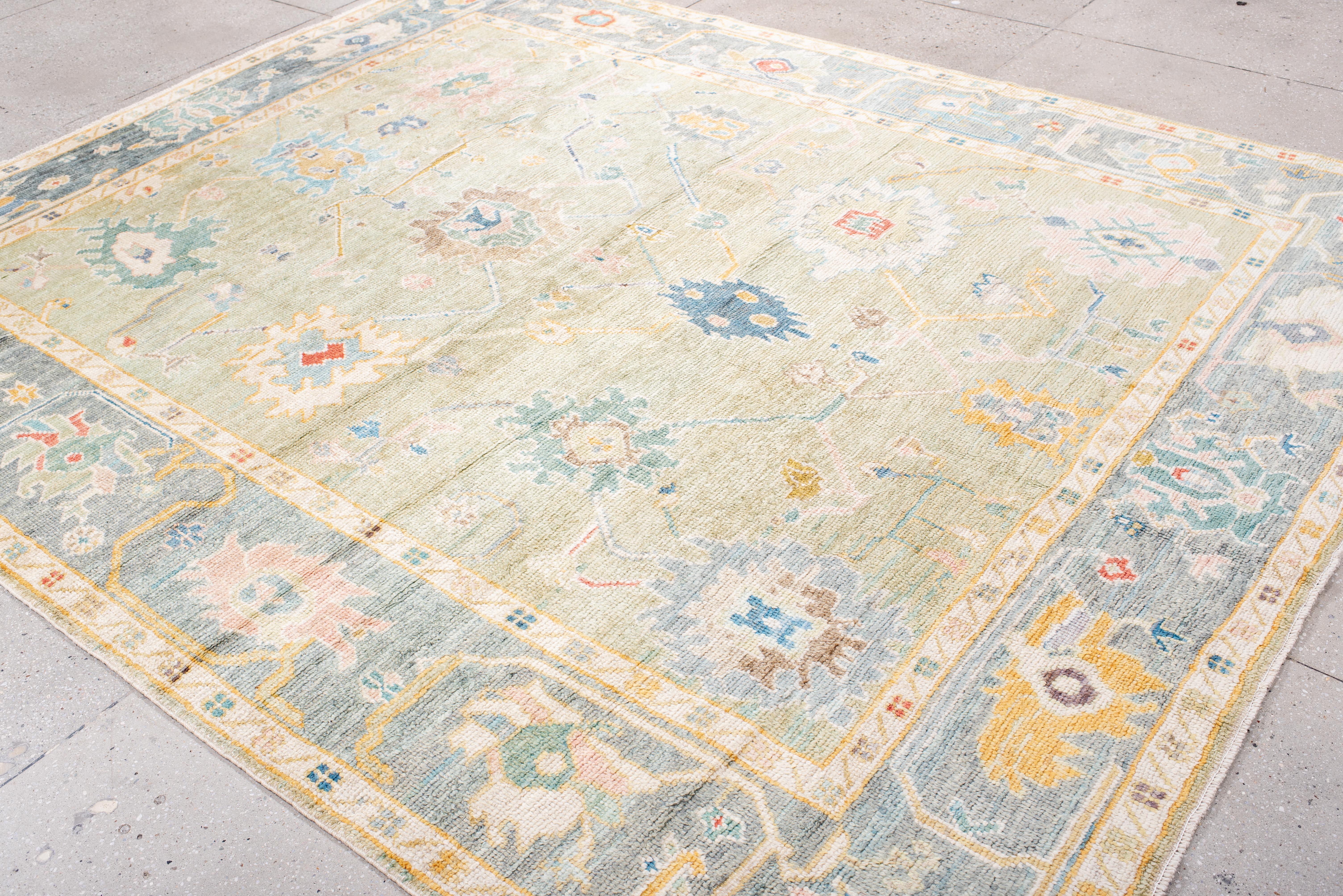 Ein spielerisches Gleichgewicht zwischen Symmetrie und Spontaneität. Dieser Oushak-Teppich ist mit verstreuten botanischen und geometrischen Motiven verziert, die jeweils mit einer organischen Flüssigkeit gewebt sind, die sowohl gewollt als auch