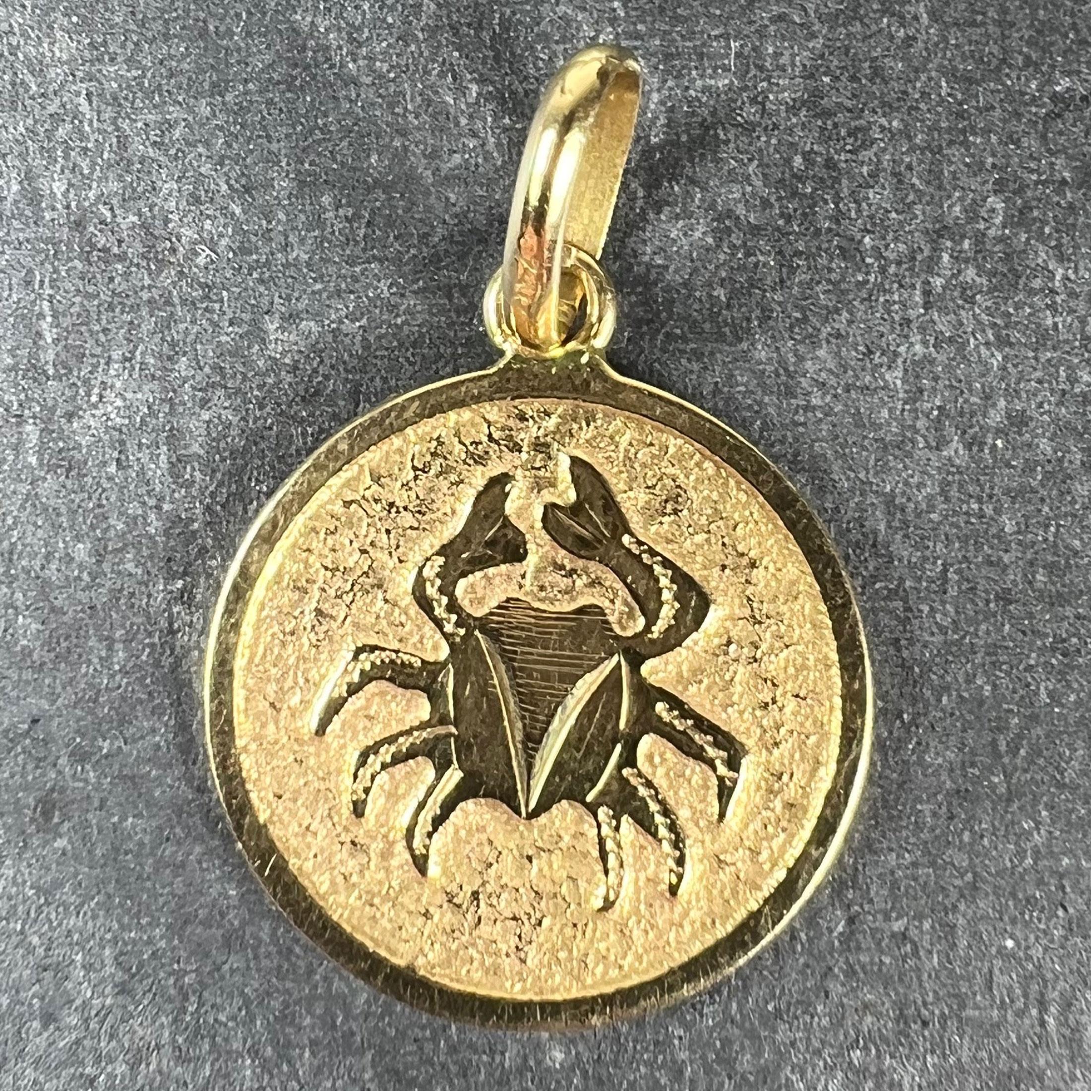 An 18 karat (18K) yellow gold charm pendant designed as a round medal with an engraved recess depicting a crab representing the zodiac star sign of Cancer. Stamped with the owl mark for French import and 18 karat gold.

Dimensions: 1.8 x 1.6 x 0.1