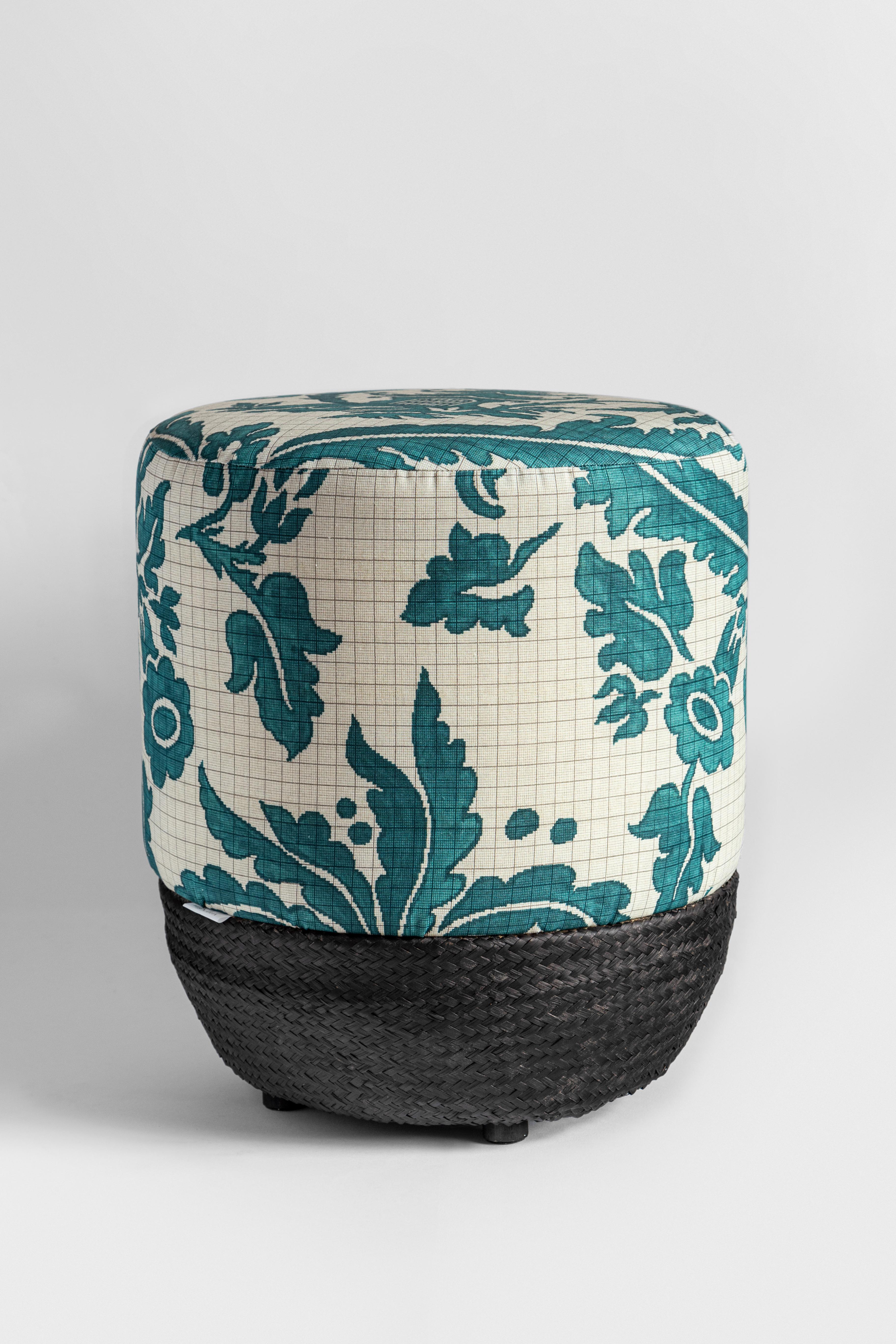 This pouf features a rather unique design: a Chinese-inspired, turquoise motif of a phoenix, a pagoda, and some fronds. These are well arranged over a delicate black squared grid that stands out on top of a white background. This style, typical of