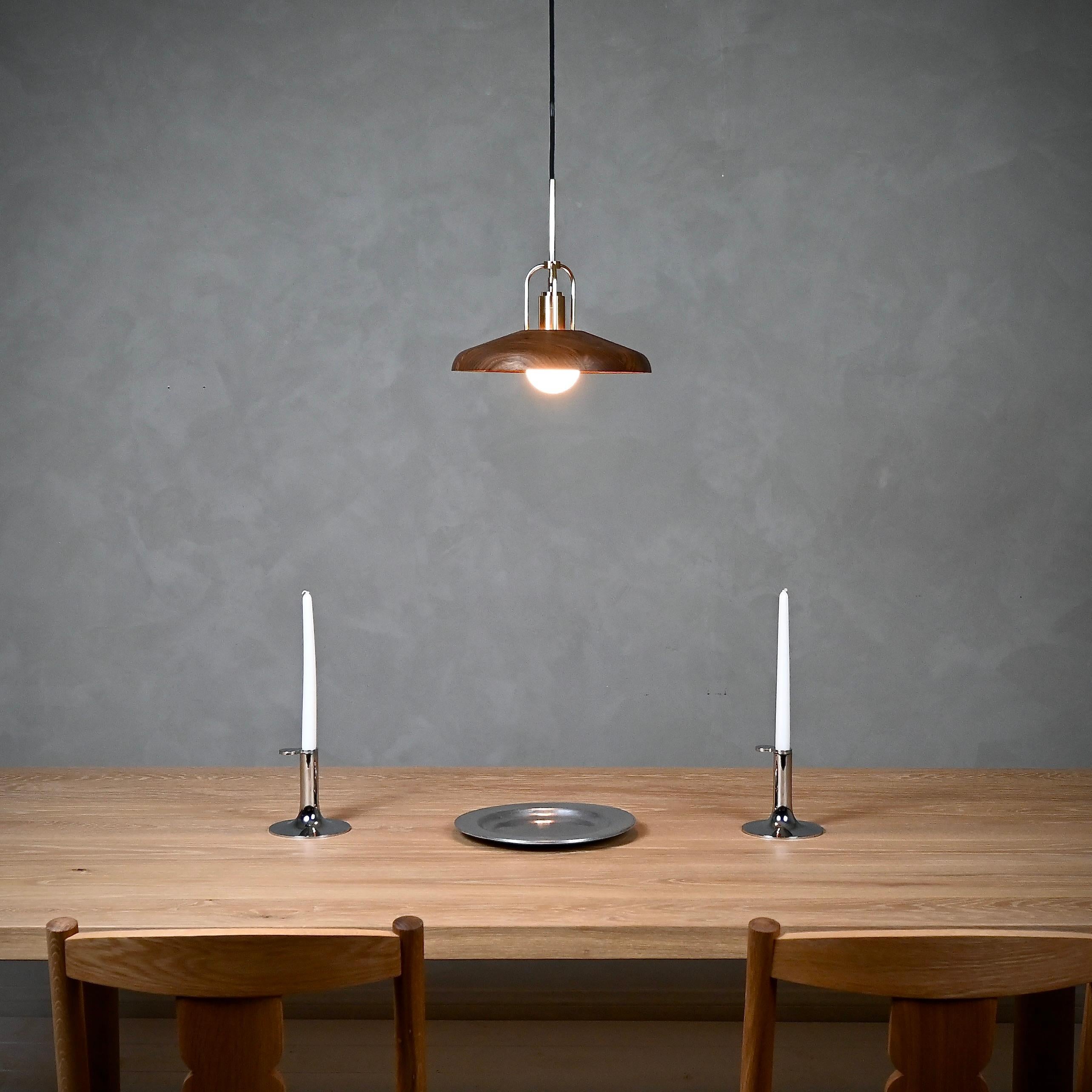 The Candela Pendant Lamp is beautifully crafted, combining refined material exploration with precise engineering. Its shade, meticulously milled from black walnut or white oak, showcases the wood’s stunning natural grain. A light bulb elegantly