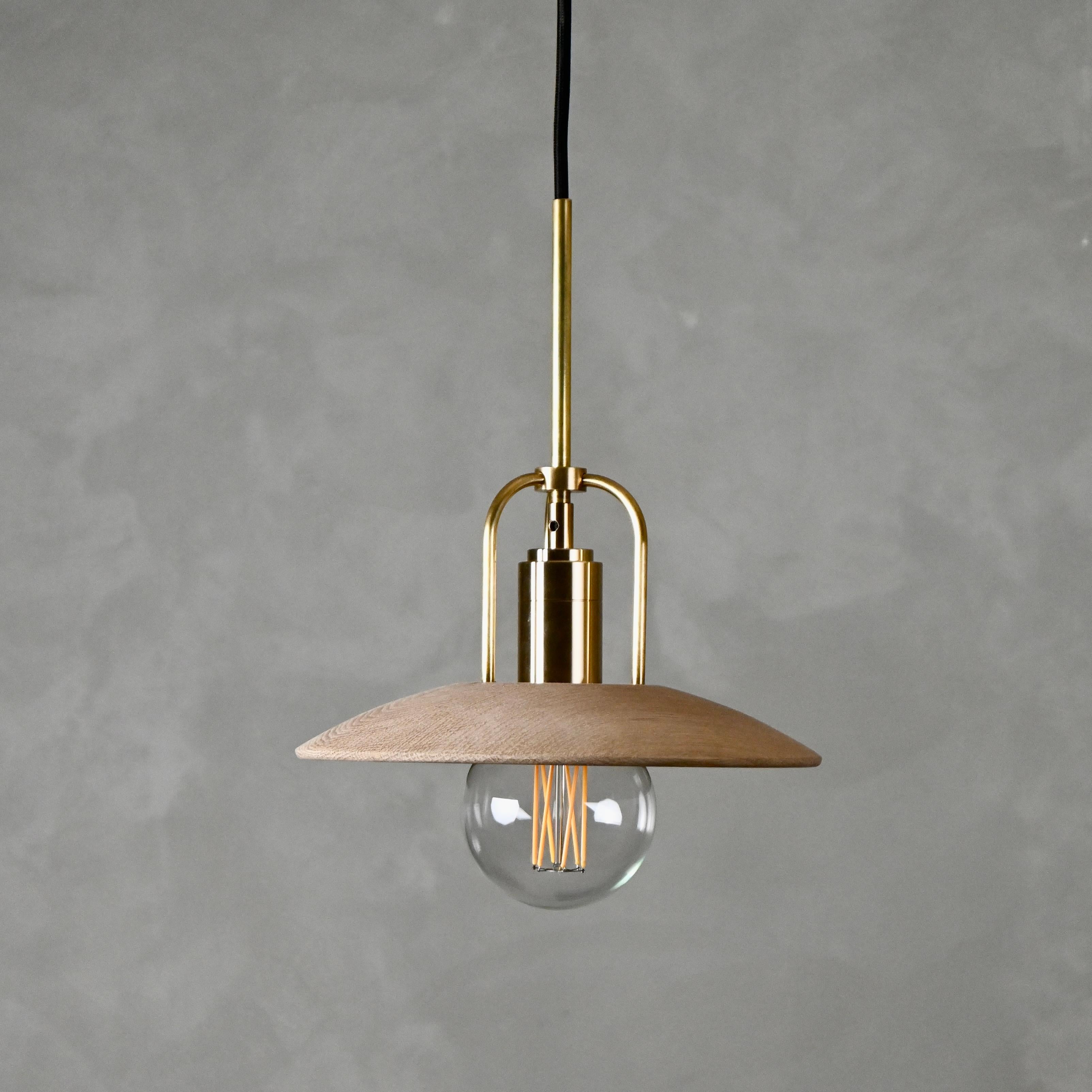The Candela Pendant Mini is a beautifully crafted light fixture that highlights the richness of solid hardwood, meticulously milled to reveal its natural grain. A light bulb is suspended through the top opening, casting a warm glow on the solid