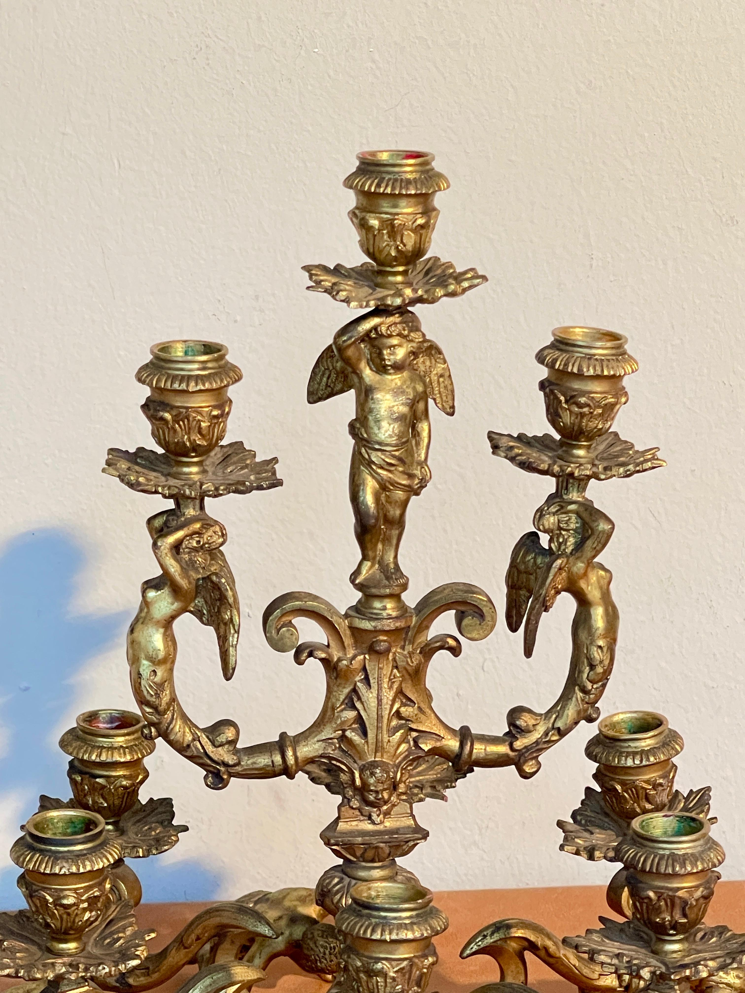 Magnifico candelabro d'epoca in bronzo dorato, finemente cesellato, presenta una struttura riccamente decorata e sostenuta da quattro putti scolpiti, raffigurati in pose dinamiche e piene di movimento. L'opera culmina in una raffinata composizione