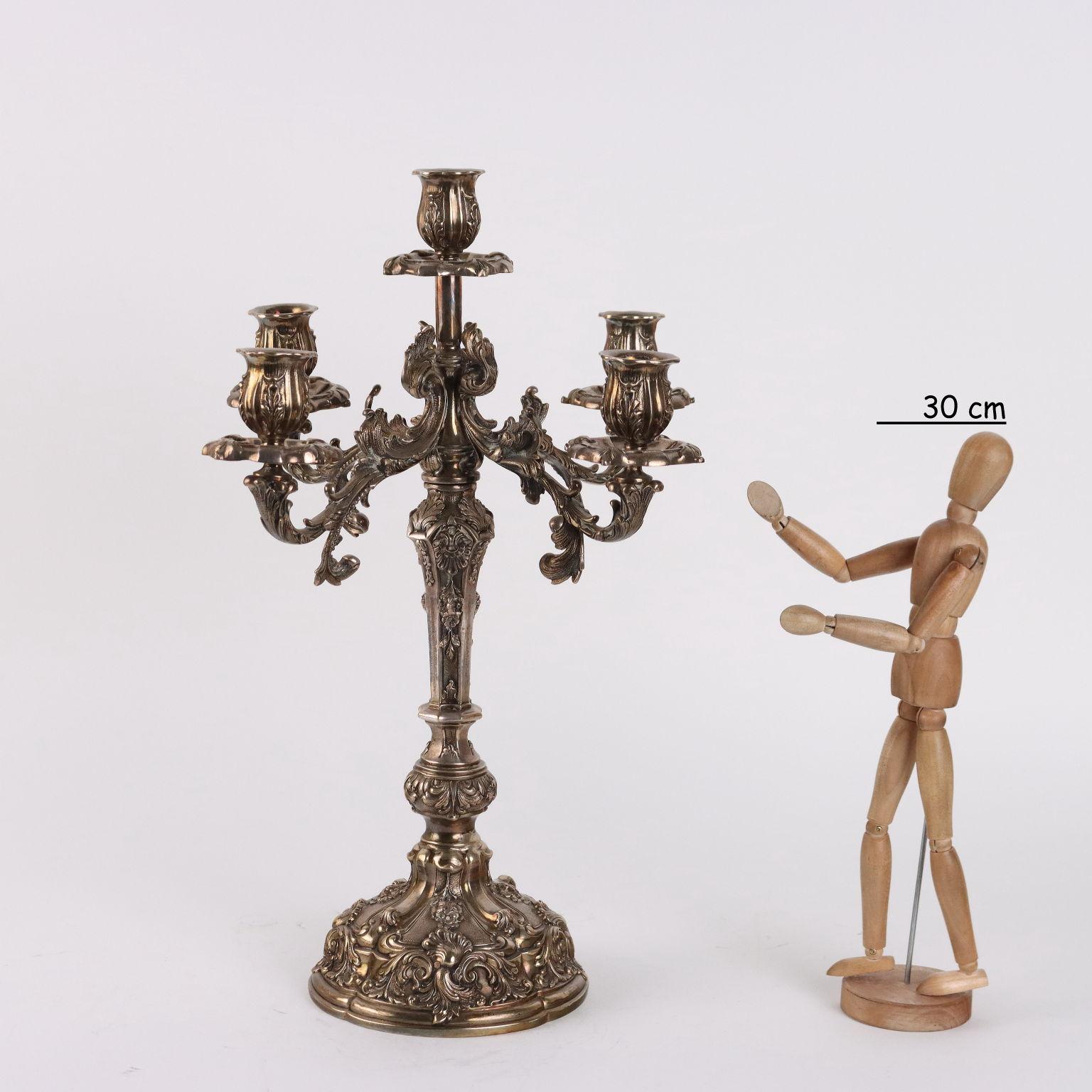 Candelabro in argento a cinque fiamme finemente cesellato e lavorato a bulino con decori a motivi vegetali e volute fogliacee. Sotto la base marchi dell'argento e dell'argentiere. Grammi 3365.
