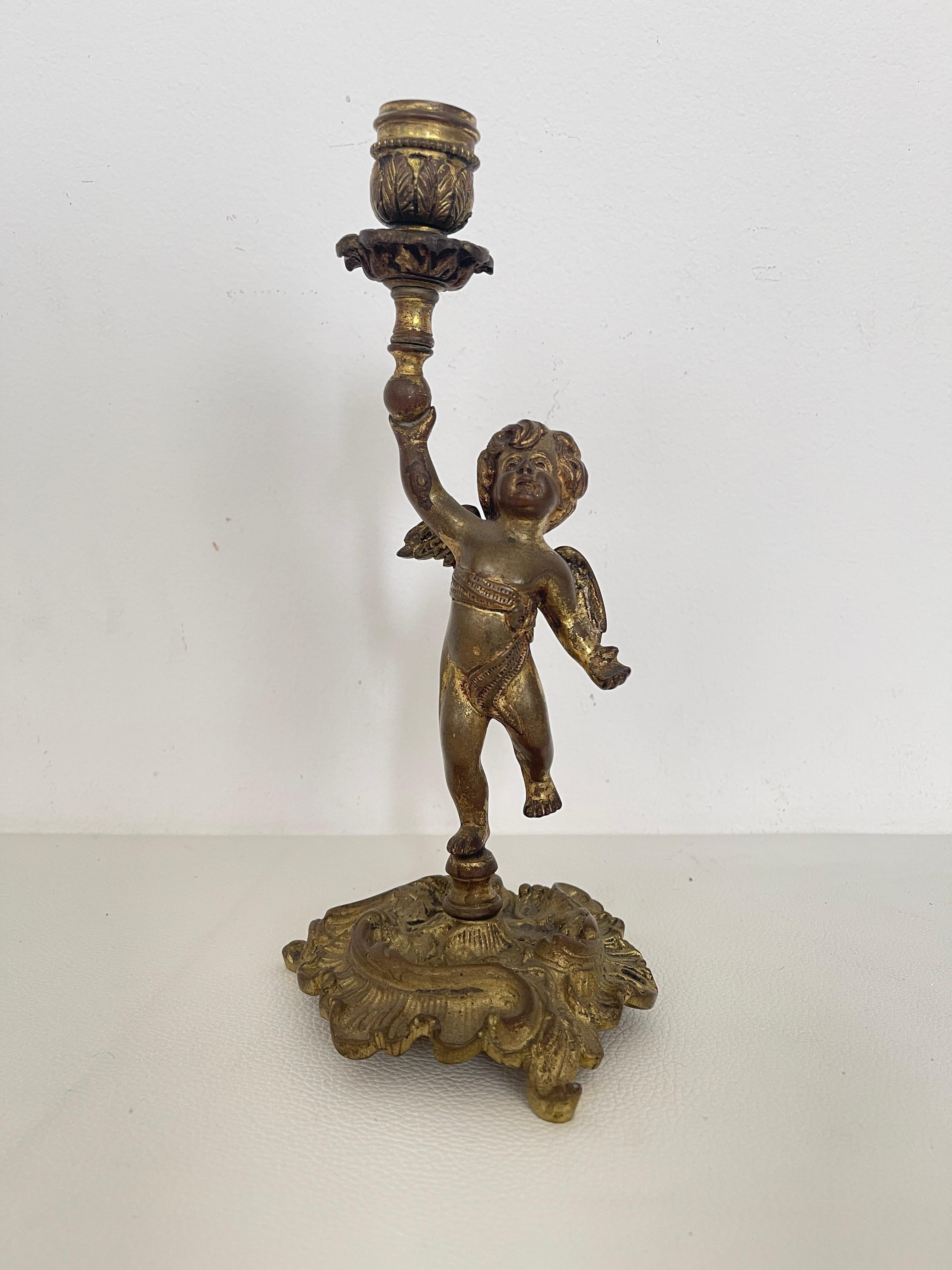 Ravissant chandelier en bronze doré, finement travaillé, représentant un putto (chérubin) ailé tenant un bras de bougie. La base, richement décorée de motifs rocaille, confère une élégance typiquement baroque à ce petit chef-d'œuvre du mobilier.

Un