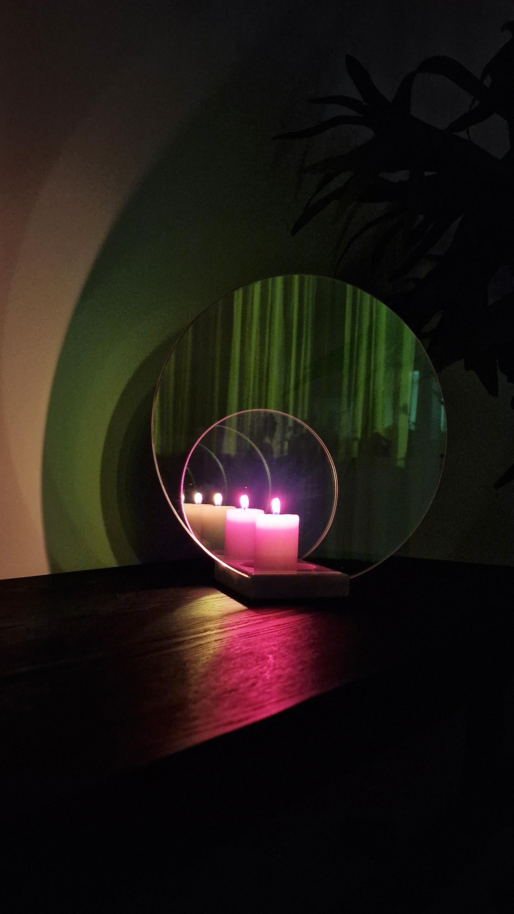 Le bougeoir offre un spectacle fascinant d'ombres colorées et changeantes qui remplissent l'espace d'une lueur chaleureuse et intime. Réalisés en verre bichromatique et en marbre, ses disques et miroirs colorés projettent un halo de lumière et de