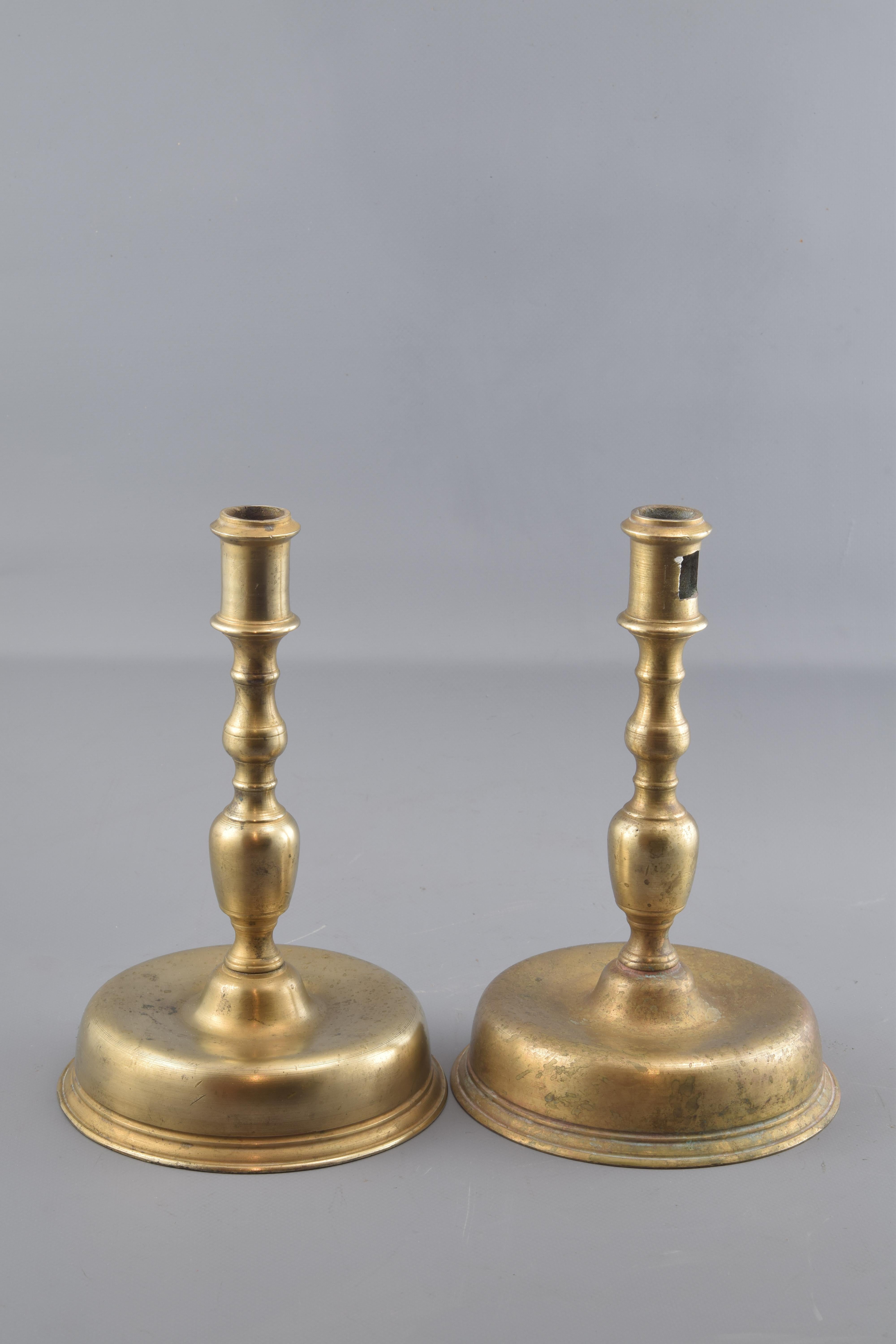Kerzenständer aus Bronze, bestehend aus einem runden Sockel, der zur Achse des Stücks hin erhöht ist, einem vasenförmigen Körper mit Zierleisten und einem Stück im oberen Teil, das die entsprechende Kerze hält. Sie sind von alten Vorbildern