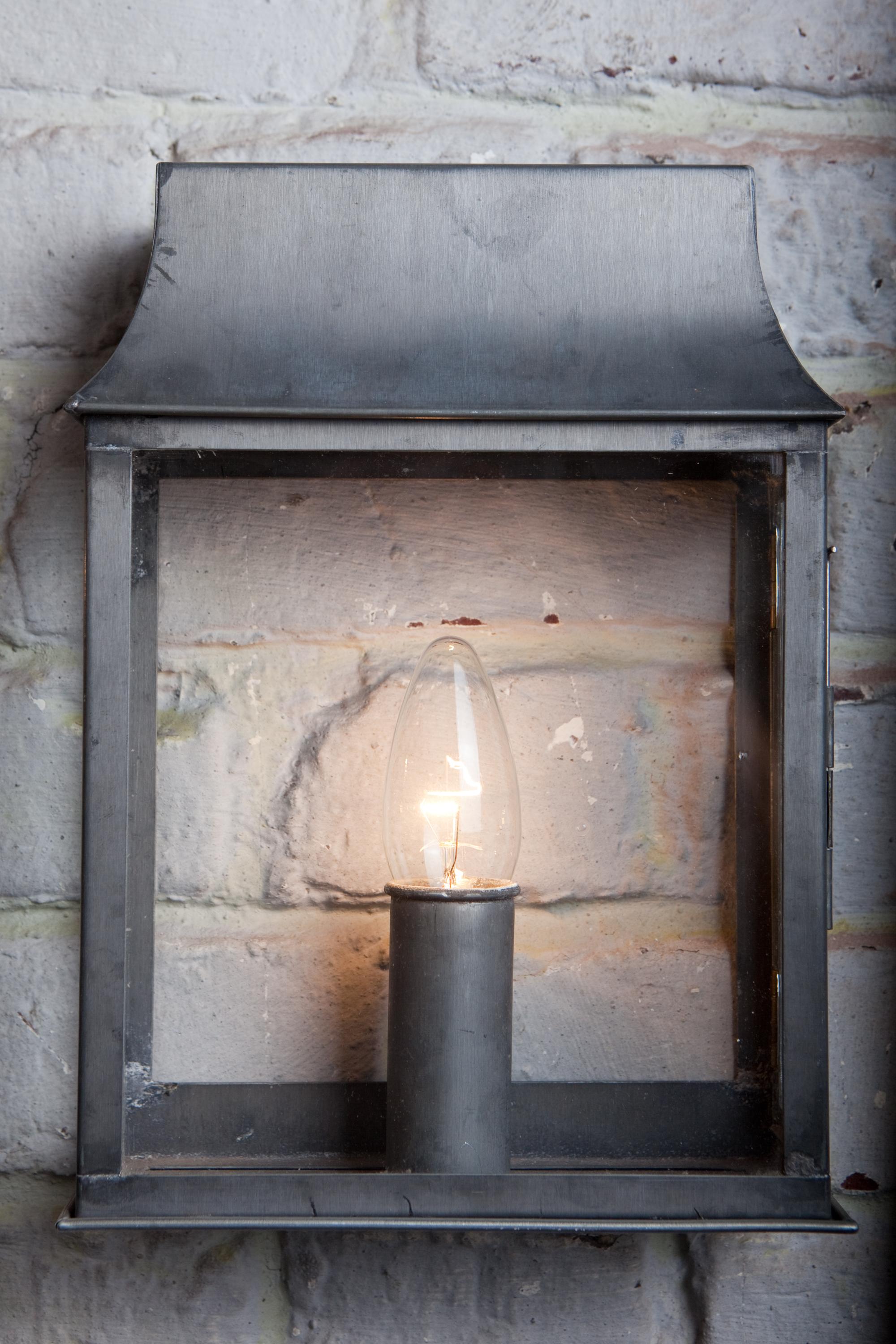 A wall fixture in zinc, glass in front, no backplate. So you can see the wall straight through. With a e14 candle lamp. 
Also available in bigger version with 2 lamps. This one only for inside use.