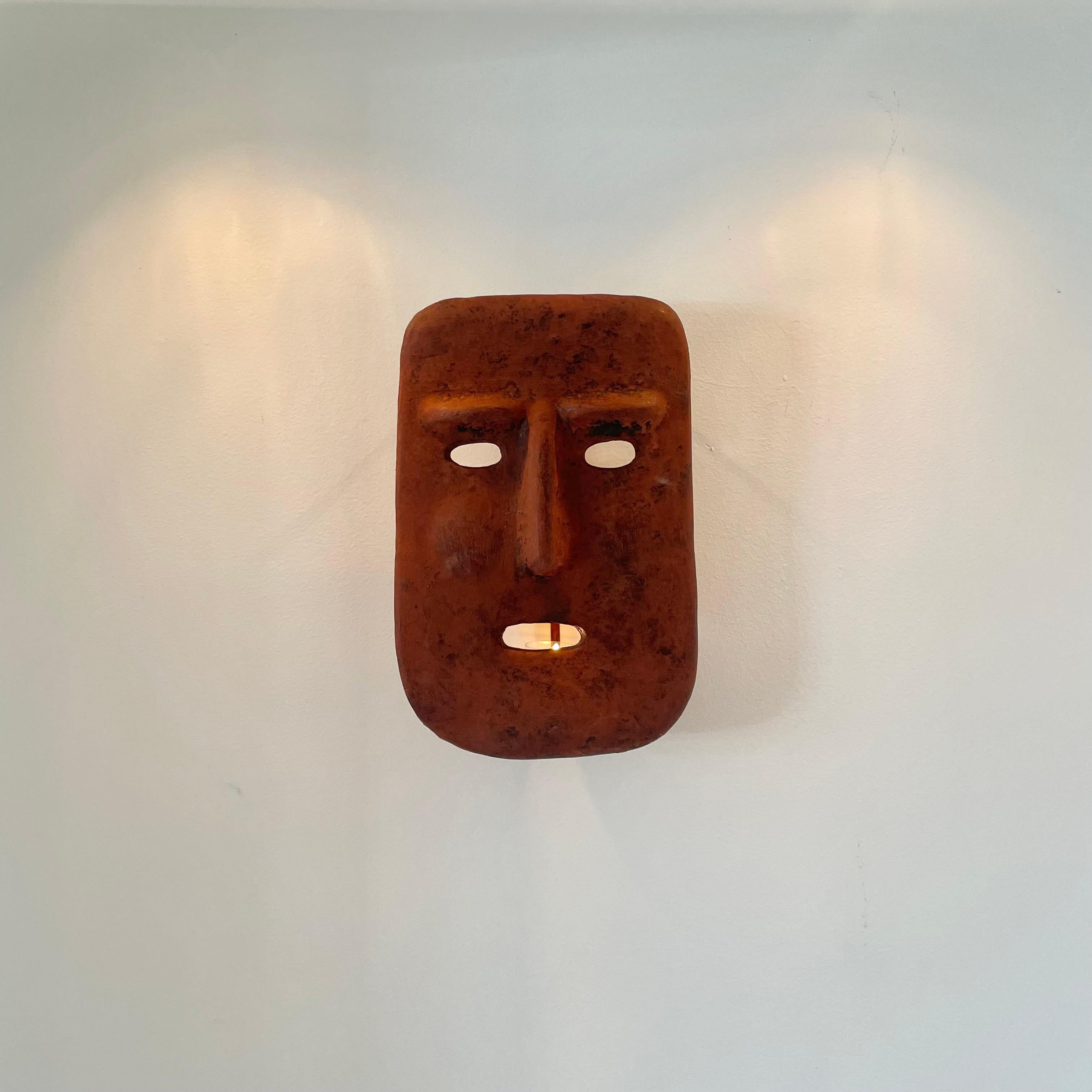 Sculptural clay mask candle sconce made in Italy. Hand made in an aged adobe color with a place for a single candle inside. Mask has a metal frame which gives the piece a nice depth from the wall and provides a surface for the candle to sit on.