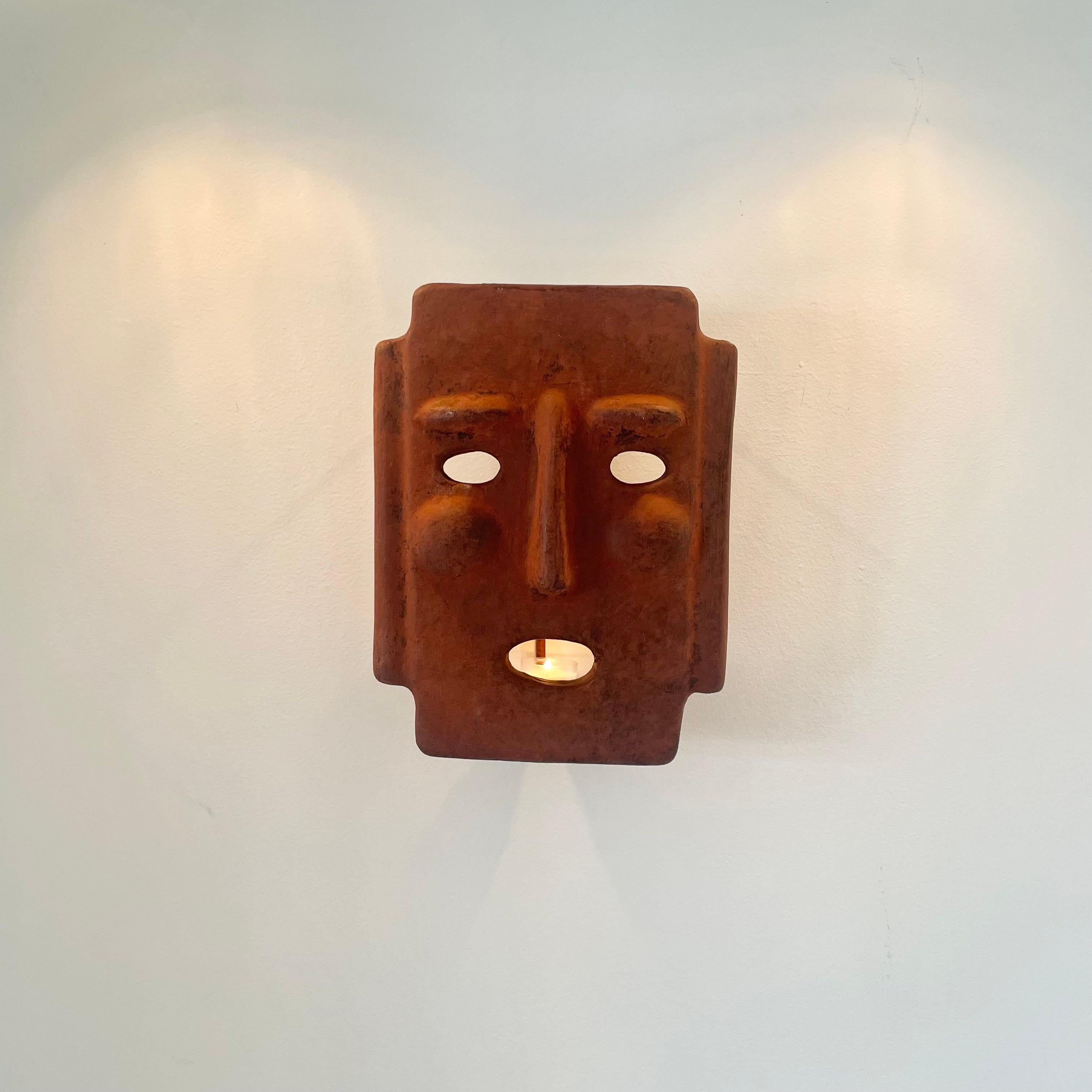 Fantastique applique de bougie sculpturale en forme de masque en argile, fabriquée en Italie. Fabriqué à la main dans une couleur adobe vieillie avec un emplacement pour une seule bougie à l'intérieur. Le masque est doté d'un cadre en métal qui