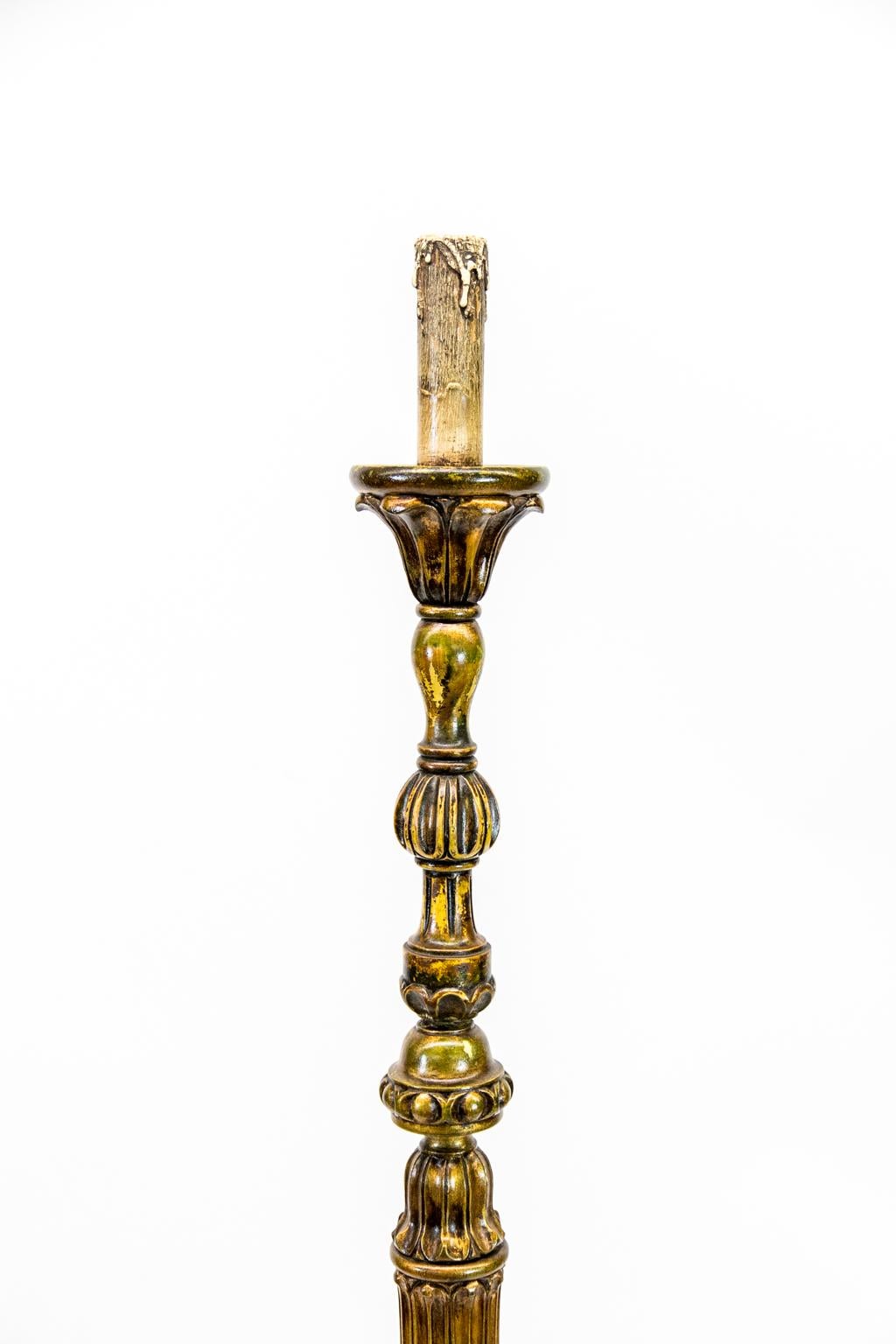 This candle stand/floor lamp has a stem with various carved motifs in the upper section. The center area is fluted and terminates in a stylized acanthus leaf base that rests on a triple concentric ring platform. The base has three scrolled shaped