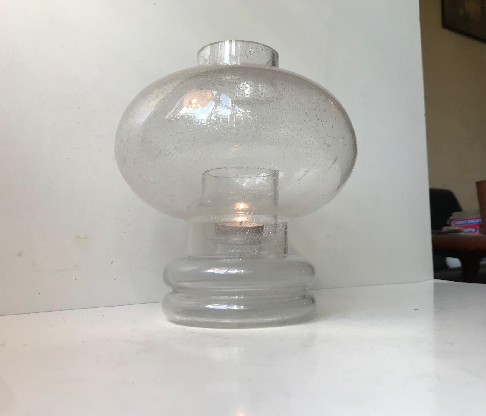 Räumlich wirkende Kerzentischlampe für Teelichter, Block- oder Kugelkerzen. Sie hat einen Sockel aus klarem mundgeblasenem Glas und einen Schirm aus klarem Blisterglas. Entworfen von Nanny Still in den späten 1960er Jahren und hergestellt von