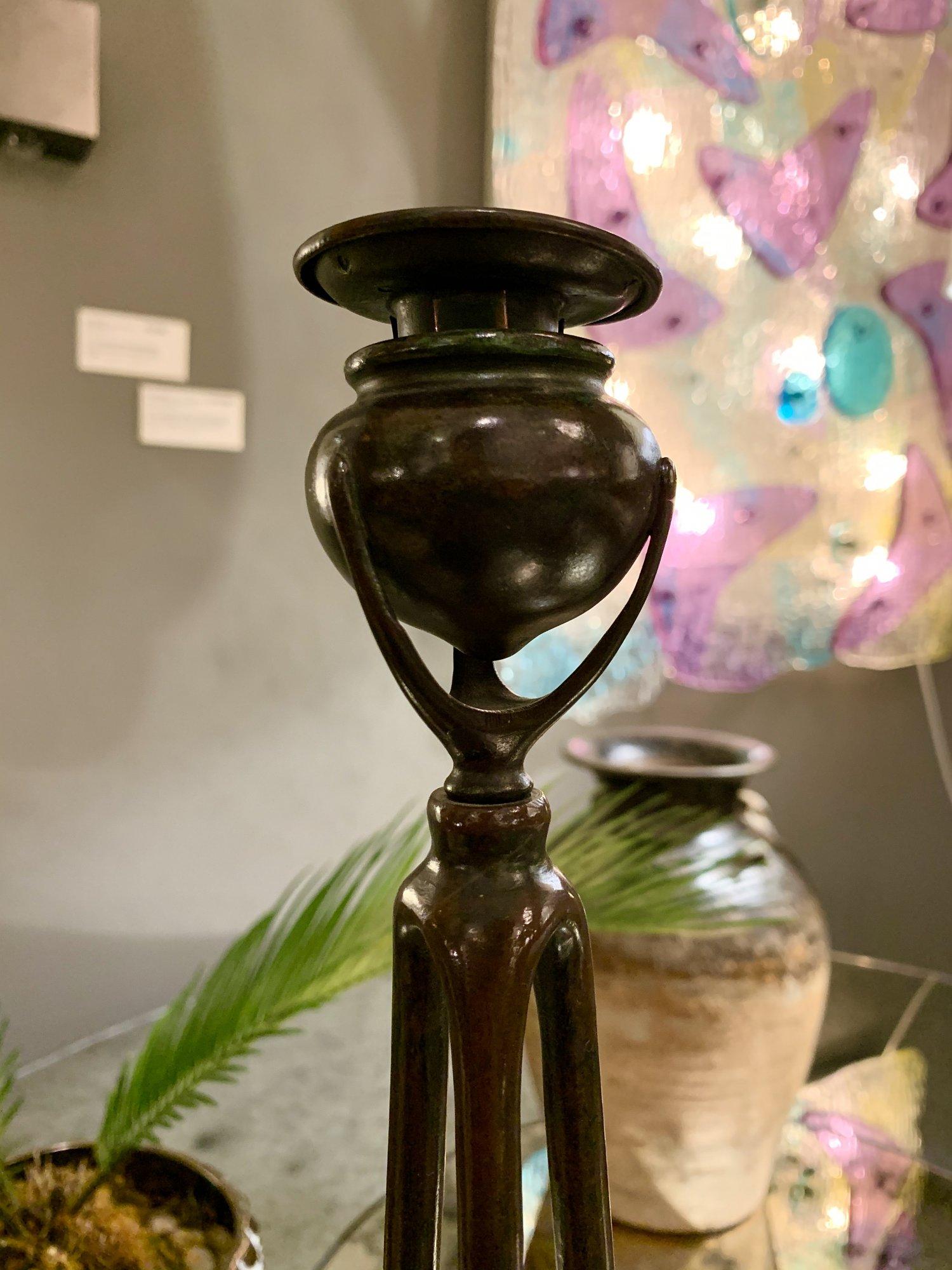 Patinierte Bronze mit Verdigris-Passagen, bestehend aus drei Streben, die einen vasenförmigen Halter tragen und den originalen bronzenen Snuffer umgeben. Auf der Unterseite gestempelt Tiffany Studios NEW YORK 10057.


