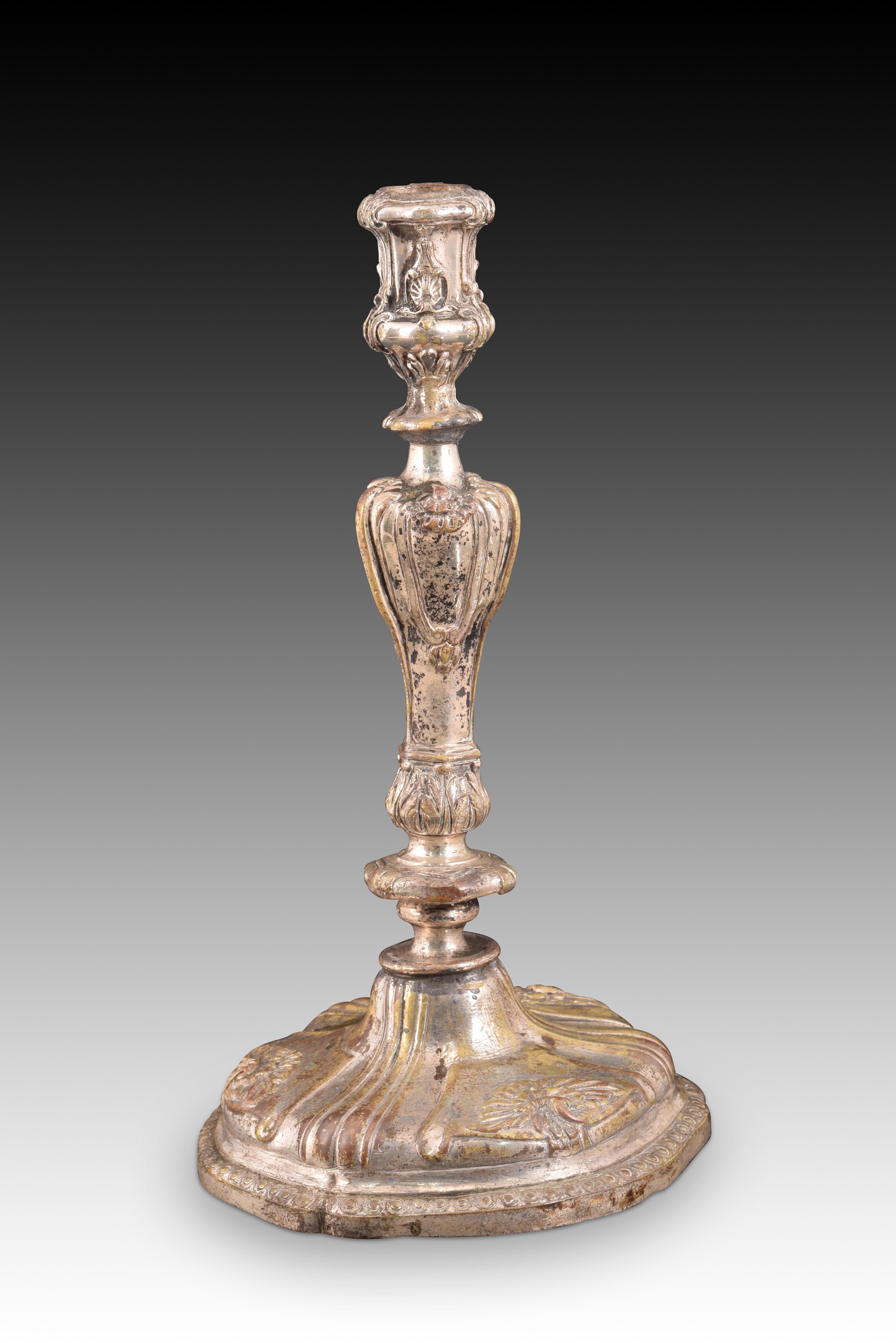 Candlestick or candle holder. Bronze. 19th century.
Bronze candlestick decorated with vegetal and venerated elements in light relief. Both the base and the axis or balustraded foot with a disc and the upper part present a series of curves in their
