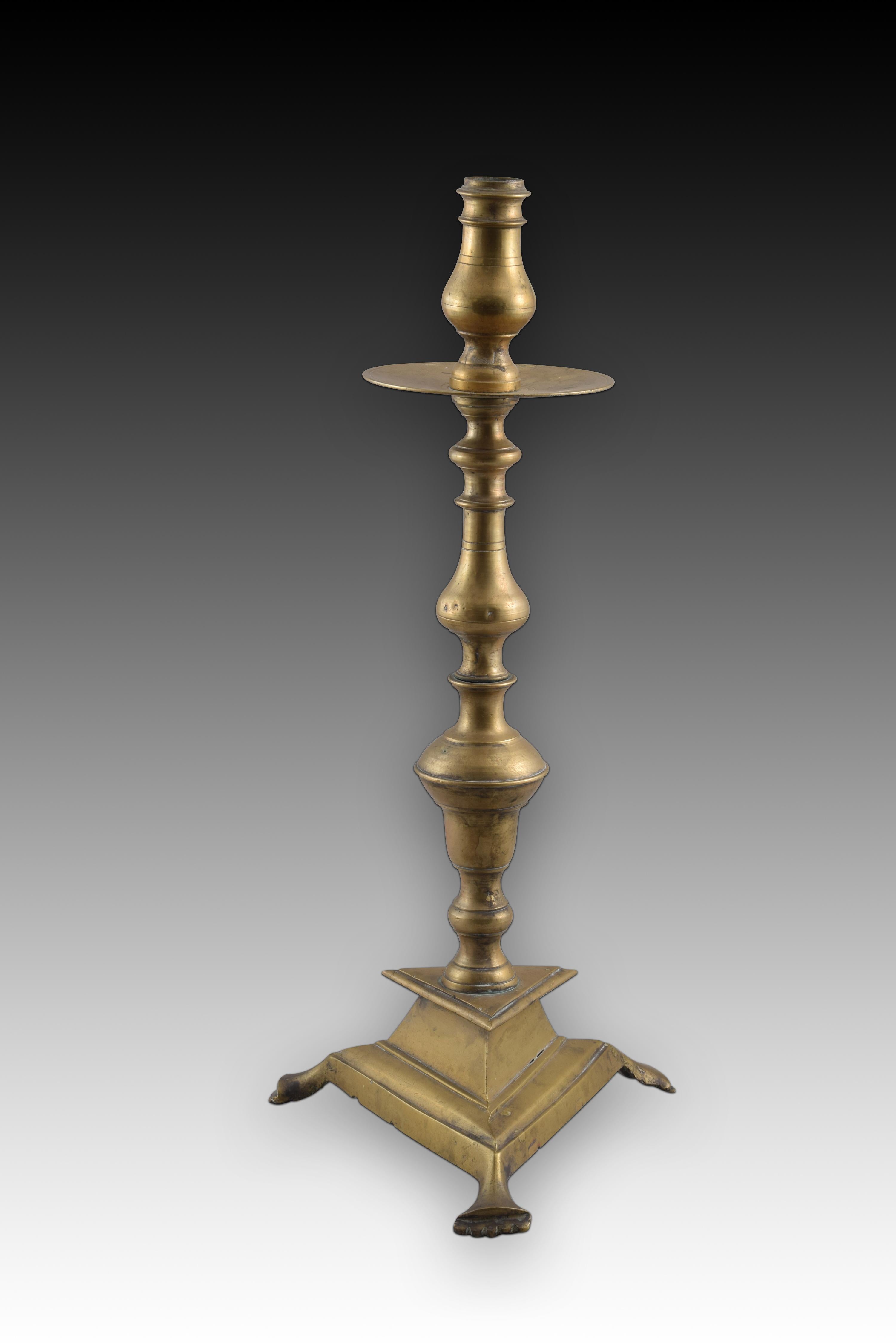 Candlestick with triangular base. Bronze. Spain, 18th century. 
Bronze candlestick with a triangular base raised on three legs and enhanced with moldings, a balustraded shaft with discs of different diameters and a similarly decorated top, right in