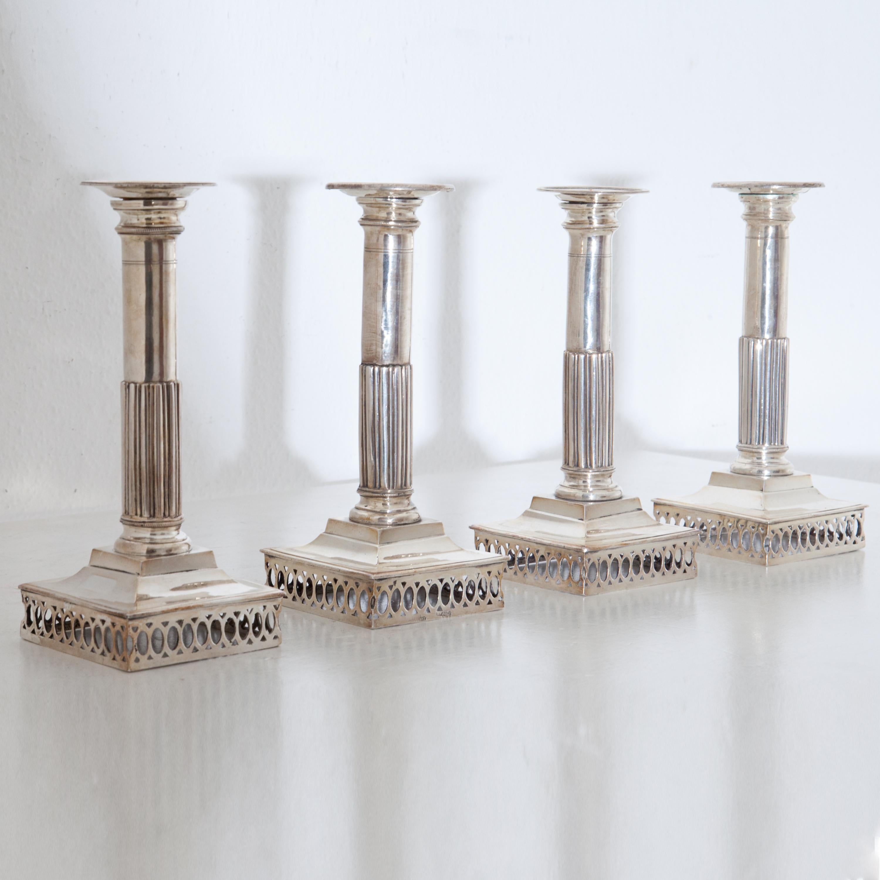 Set of four silver candlesticks on square openwork base and column shaft with pipes on the lower half. Hallmarked at the foot. Total weight: 1875 g.