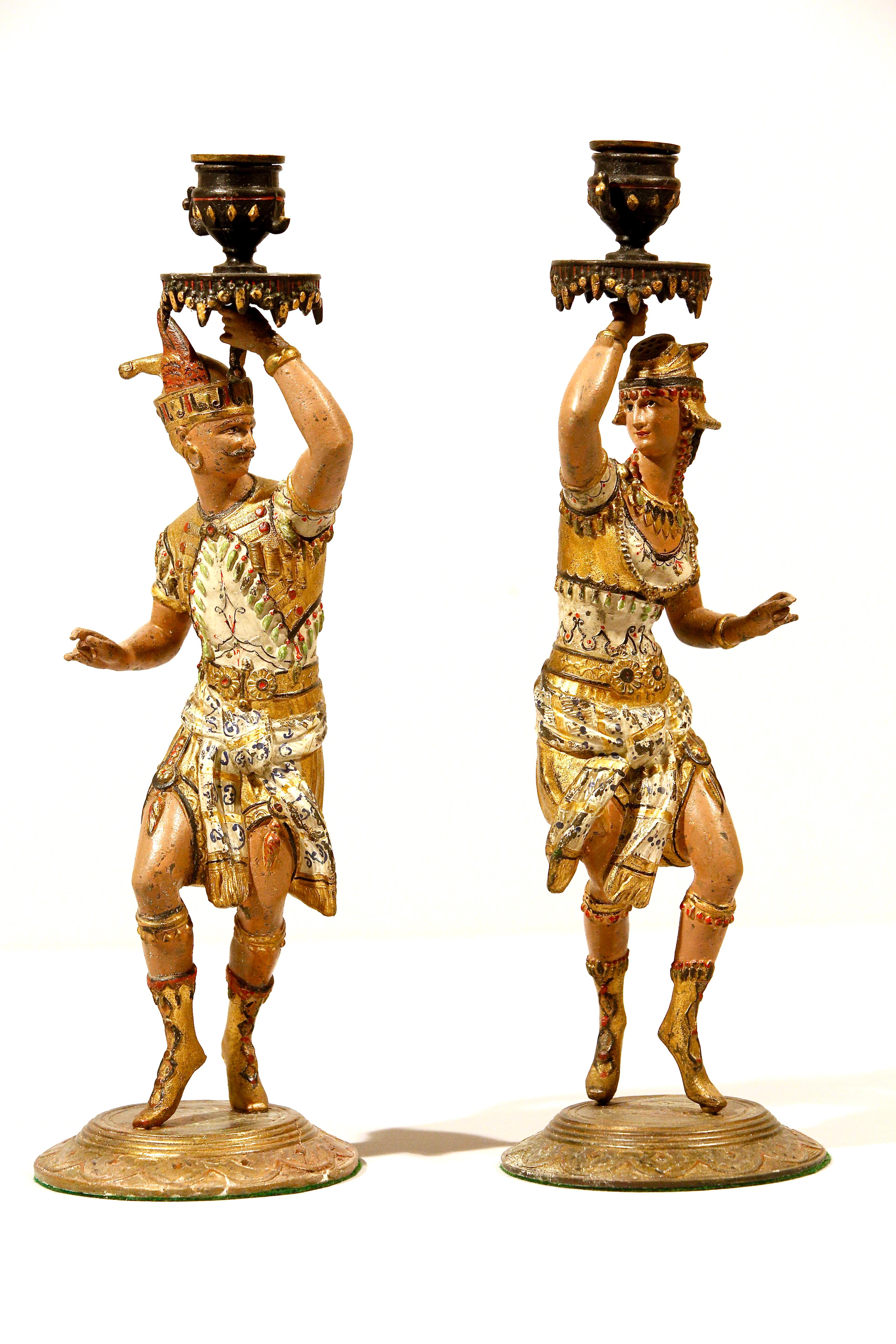 A pair of French cold painted spelter candlesticks modeled as a male and female running torch bearers in gilt highlighted  Nubian costumes, original worn paint and natural patination holding a candle holder above their heads. 

Condition excellent