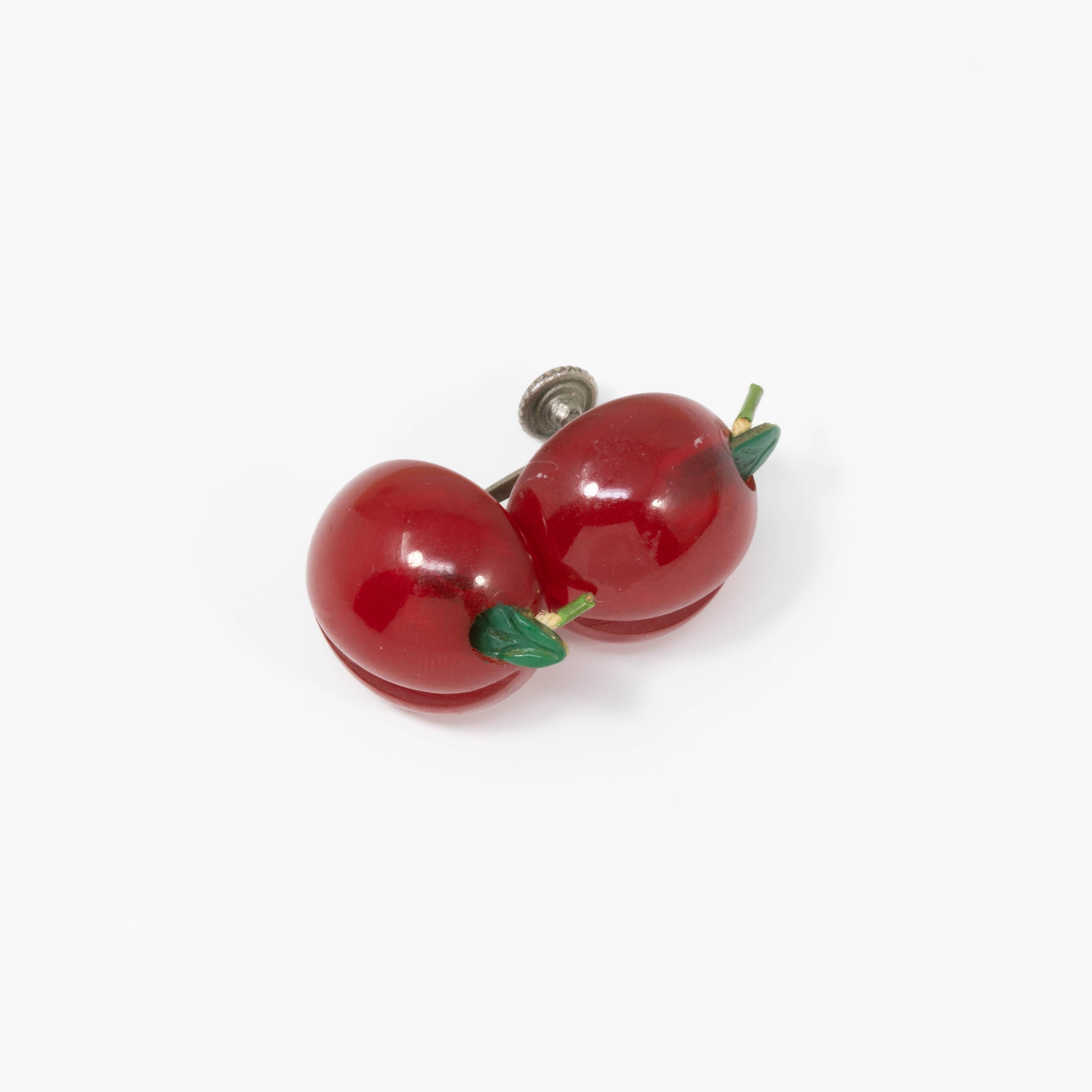 A pair of retro bakelite earrings. Each earring features candy apple red bakelite buttons accented with green leaves, set on vintage silvertone screw back findings.