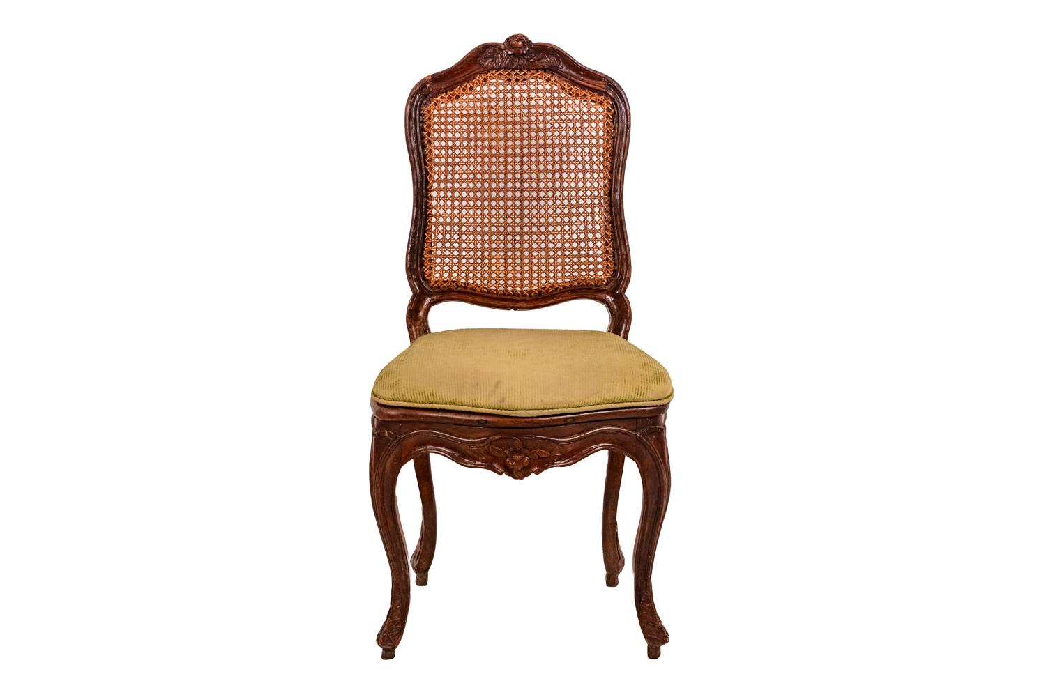 Cane chair in beech standing on four cabriole legs adorned with acanthus leaves finished by a small shoe. Scalloped apron, adorned with flowers in its center. A la Reine back with curved edges adorned with vegetal scrolls and flowers on the central