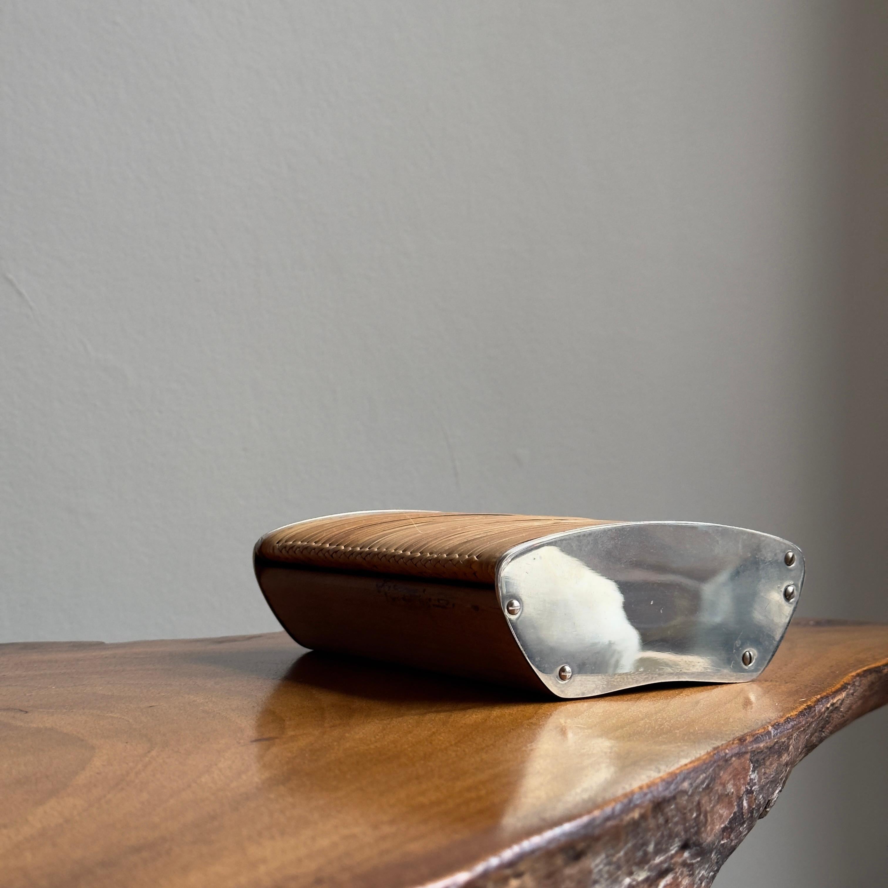 A walnut cigarette box with chrome-plated brass sides and cane wrapped lid. 

Designed by Carl Auböck II during the 1950s, cane, wood, and brass elements combine to create this beautifully tactile, functional and elegant cigarette box. These