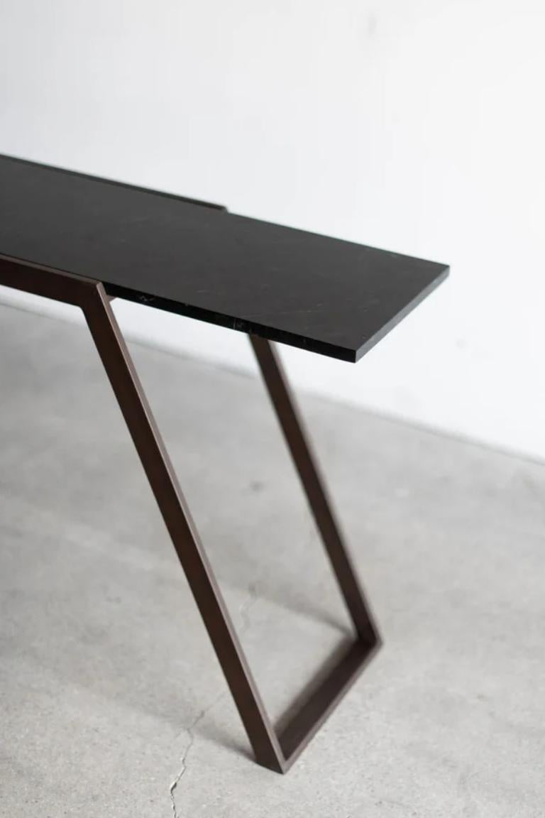 The Cane Console is a study in clean lines and angles. Its modern design features a steel frame finished with an antique bronze patina, adding warmth and depth to the piece. The console's top is a 3/4