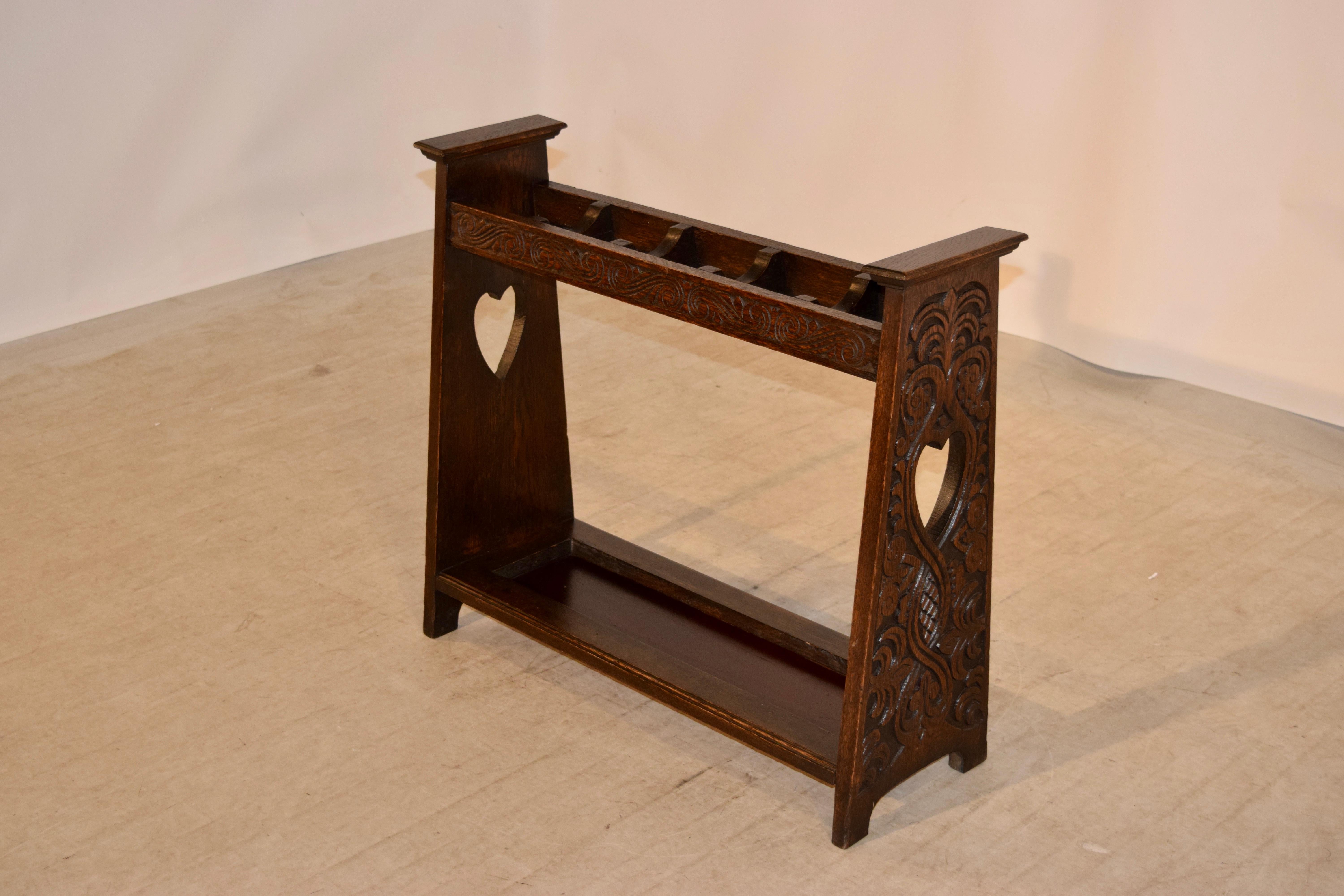 English oak cane stand in the Arts & Crafts style. The sides of the piece are heavily carved and have cutout heart shapes in the centers, circa 1920s. They are joined at the bottom by a single shelf with raised edges to keep the canes in the shelf.