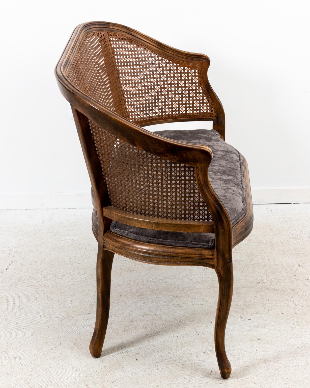 Hollywood Regency style caned back loveseat with newly upholstered seat in charcoal velvet, circa 1970s-1980s. Please note of wear consistent with age including minor finish loss to the cane and wood.