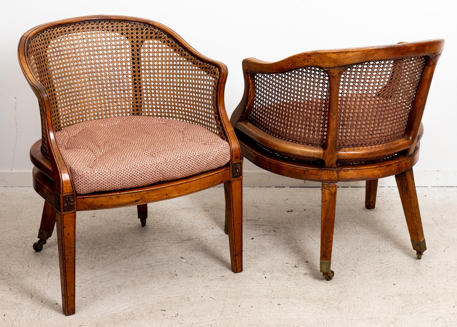 Caned back English style tub chairs on casters with tufted, upholstered seat and rounded seat back. Please note of wear consistent with age including patina and finish loss to the wood and caning.