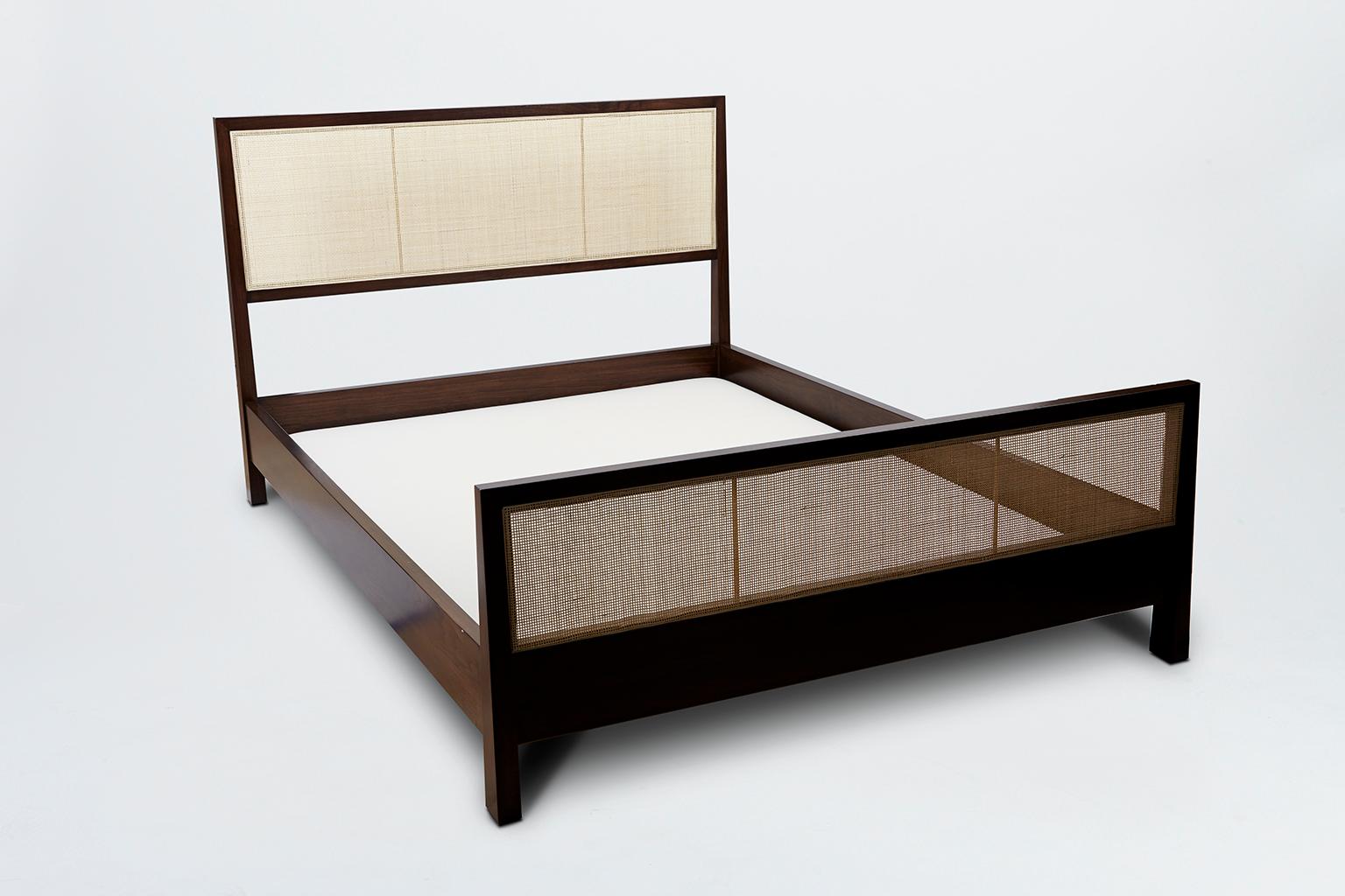The caned bed is a solid wood framed bed that can be made in either white oak or American walnut. The piece features a headboard and footboard made with natural cane inset panels and brass stretchers. Slats are provided. Shown here in Dark Walnut.