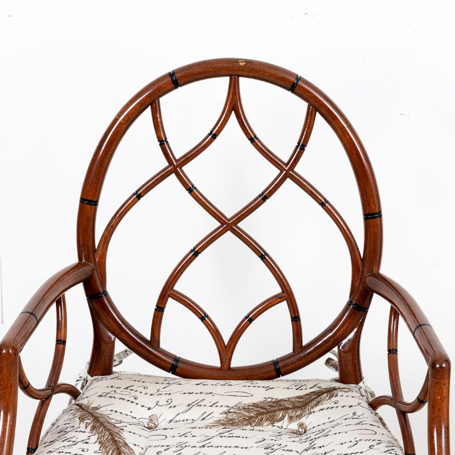 Faux bamboo painted armchair with round seat back, cane woven seat, and an upholstered cushion decorated with cursive calligraphy and feather motifs. The chair also features curved ogee shaped tracery and bottom stretchers. Please note of wear