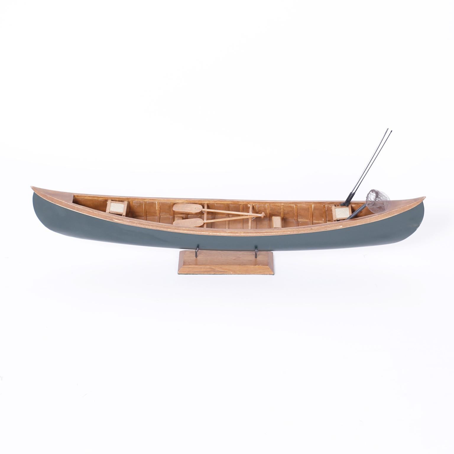 Canoe model realistically crafted in mahogany painted on the outside complete with seats, paddles, fishing poles, net and presented on a mahogany stand.