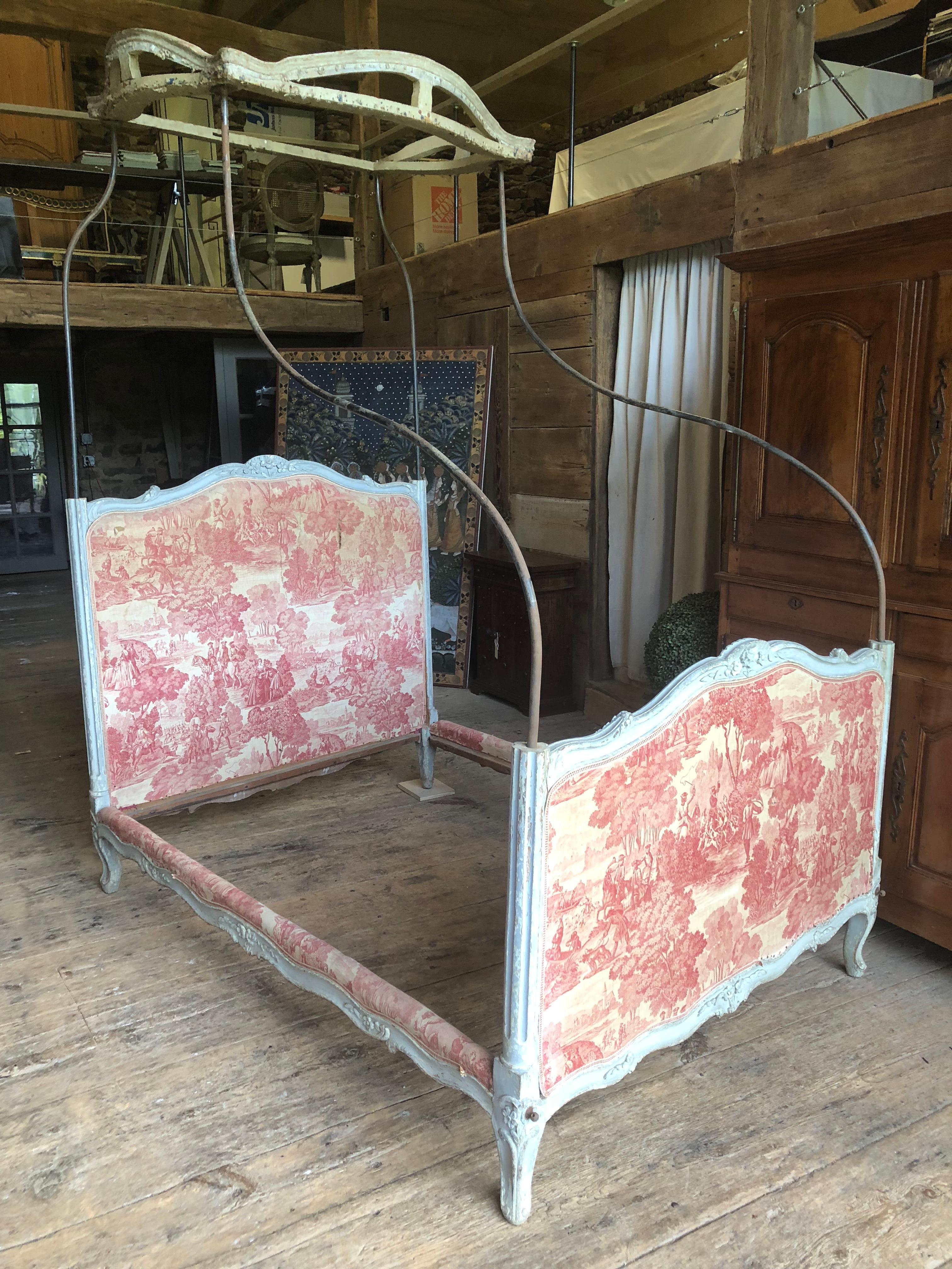 A rare 18th century Louis XV/ XVI transitional canopy bed, the crown supported by four upright curved iron rods mounted into the nicely carved grey painted frame, partially upholstered in period Toile de Jouy fabric. The bed is from the estate of