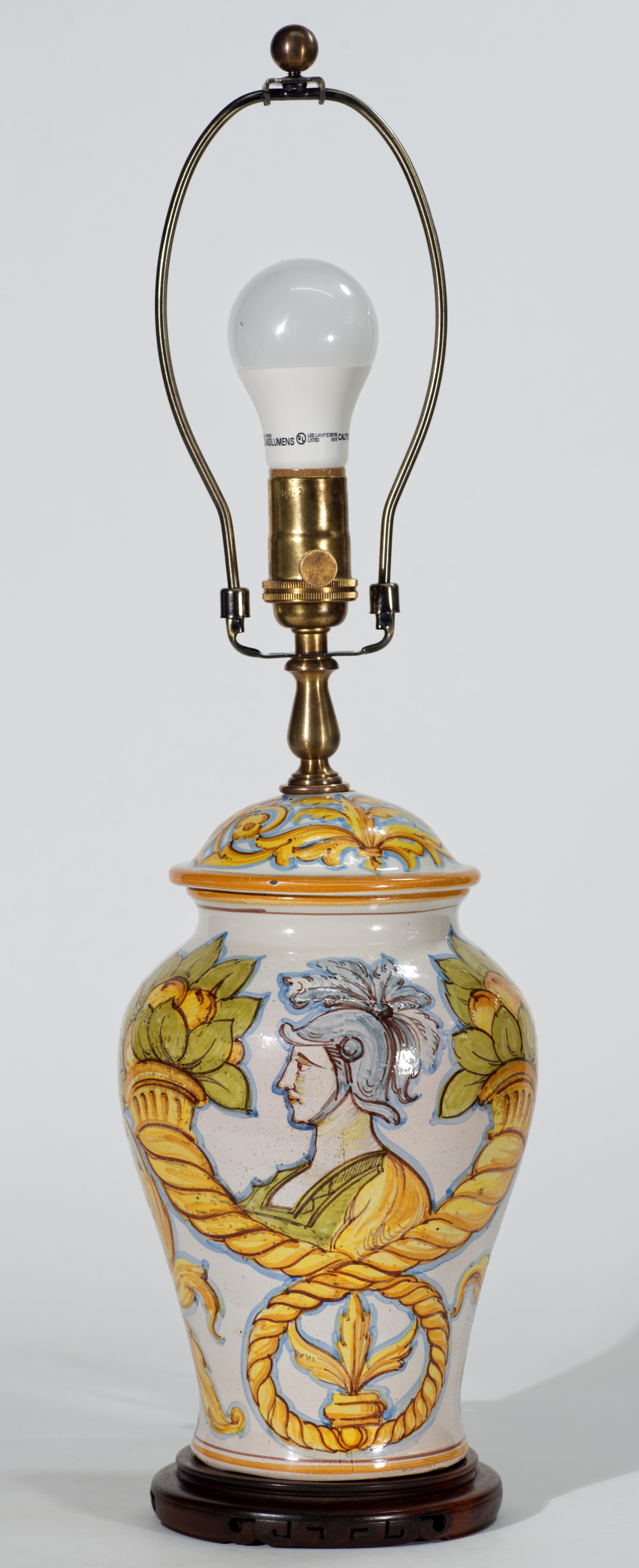  La lampada in maiolica dipinta a mano presenta il ritratto di un guerriero circondato da urne e frutti tradizionali italiani; l'altro lato presenta un disegno astratto nella stessa gamma di colori giallo, arancione e blu. L'urna con il coperchio è