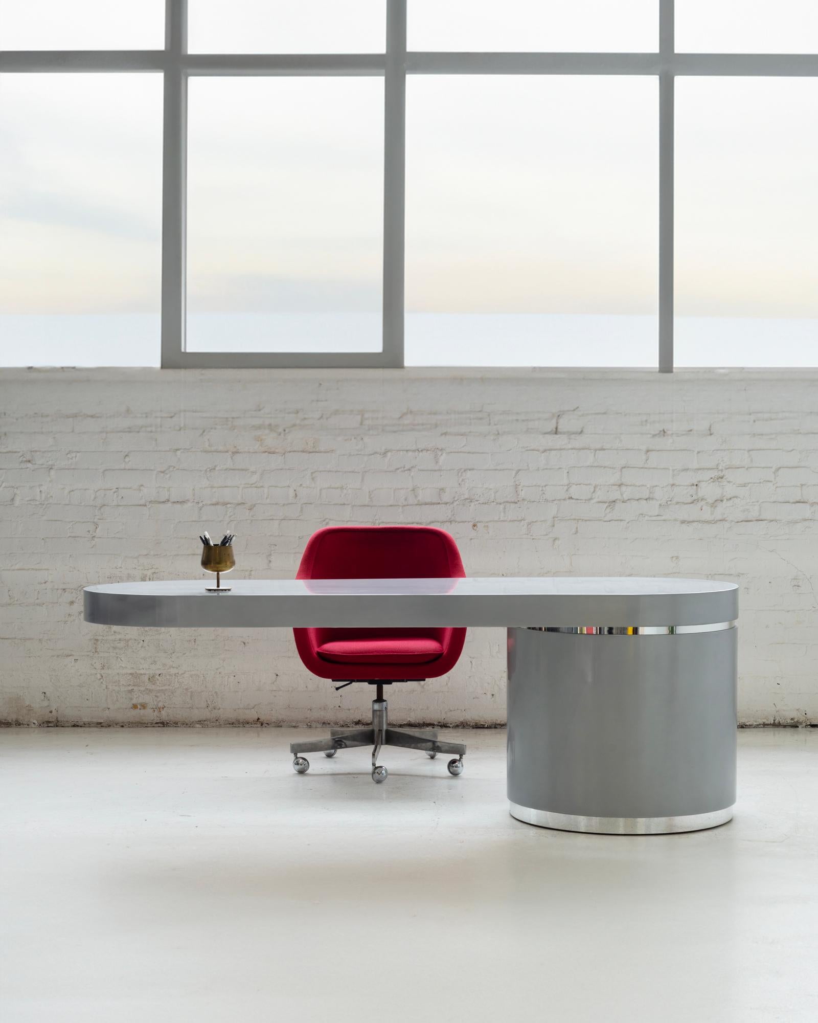 This cantilevered desk, designed by Wade Beam for Brueton, merges functionality with a sleek, modern aesthetic. It features a striking metallic silver finish complemented by polished metal accents, enhancing its minimalist charm. The desk includes a