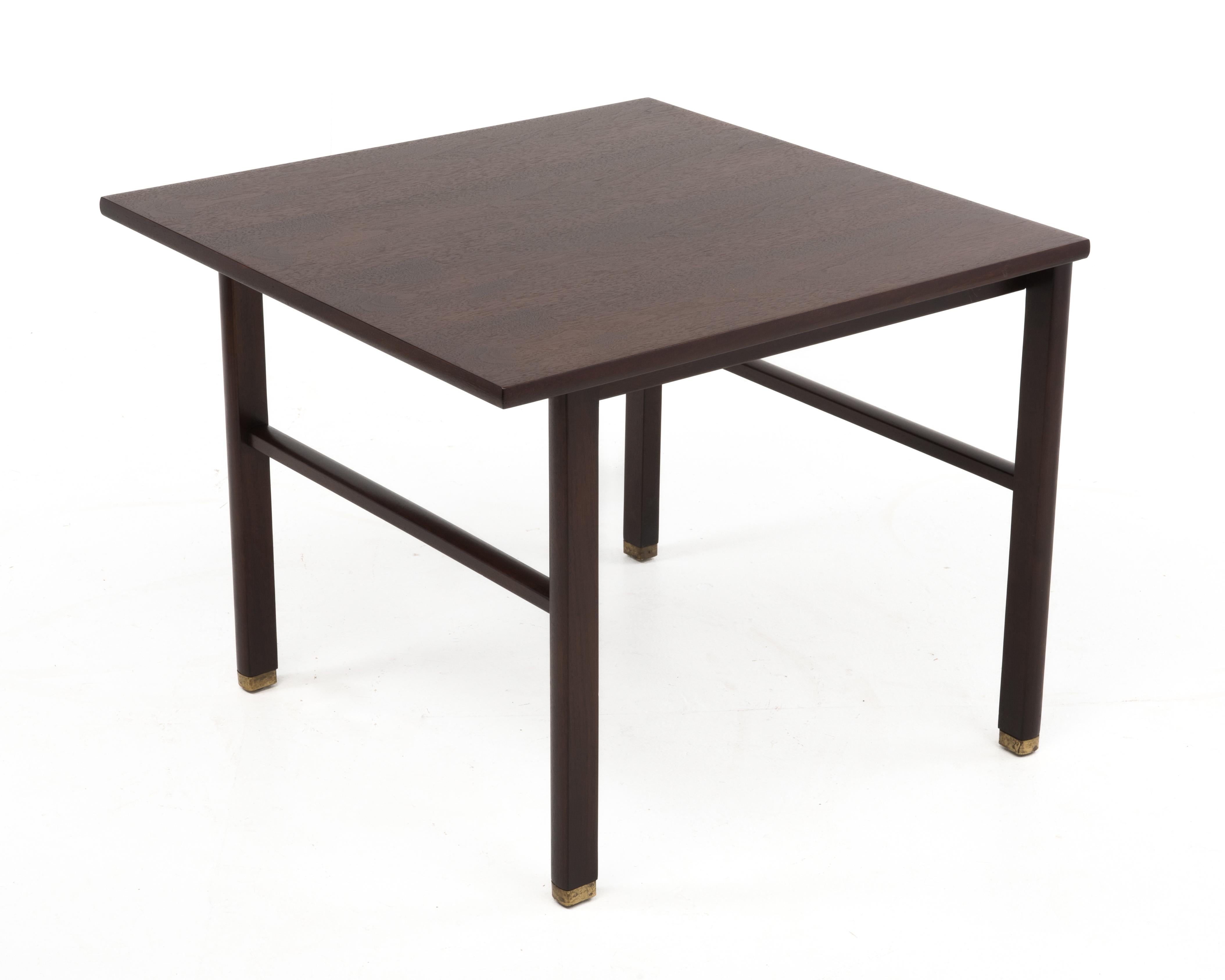 A square cantilevered walnut end table by Edward Wormley for Dunbar, c. 1960's. Features a cantilevered top and brass feet. The table retains a paper label and the original Dunbar brass tag.