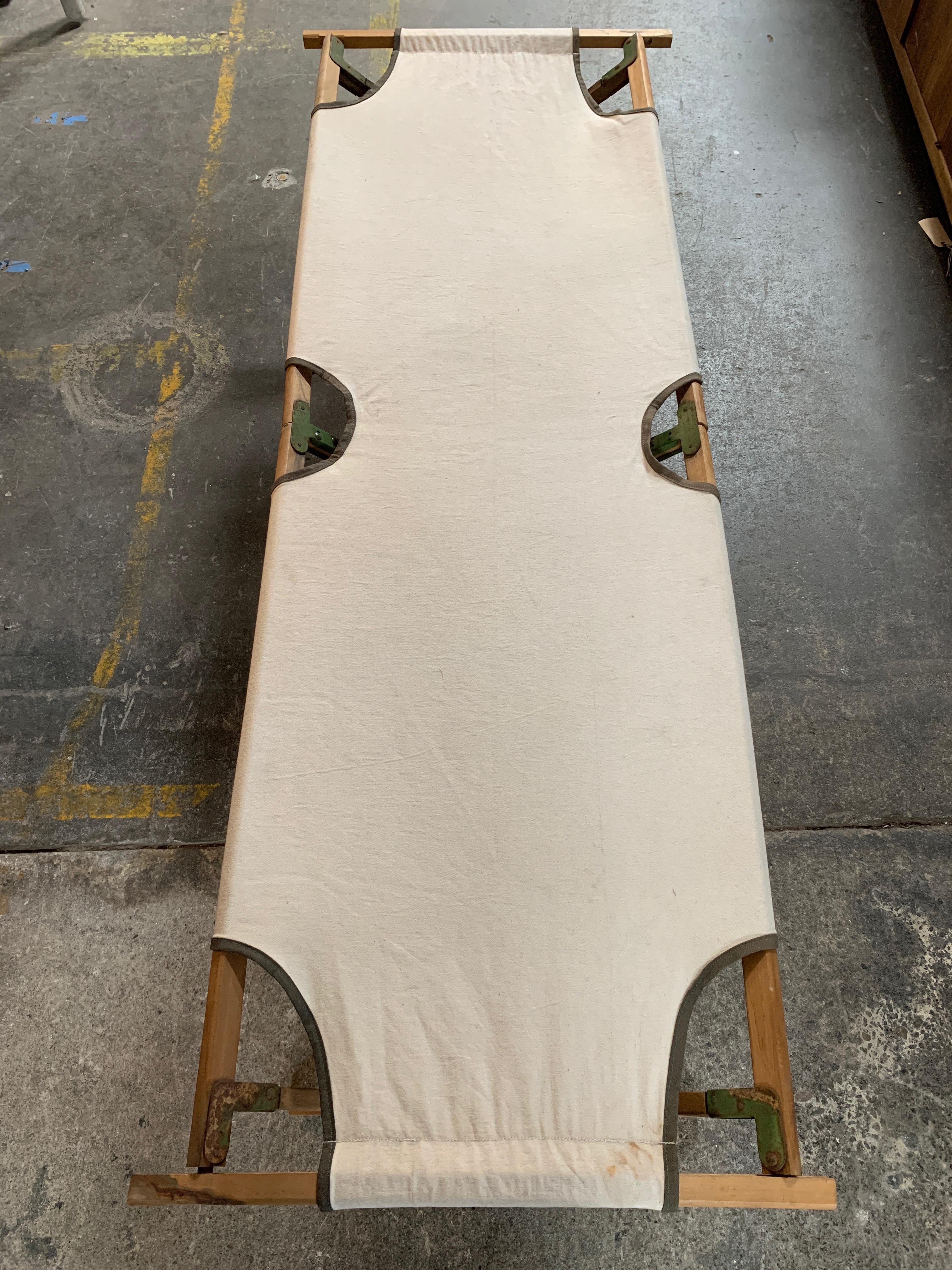 Vintage army cot, end slats removable to collapse down. Canvas fabric stretches over the wood frame creating a unique piece that carries a history only it knows.