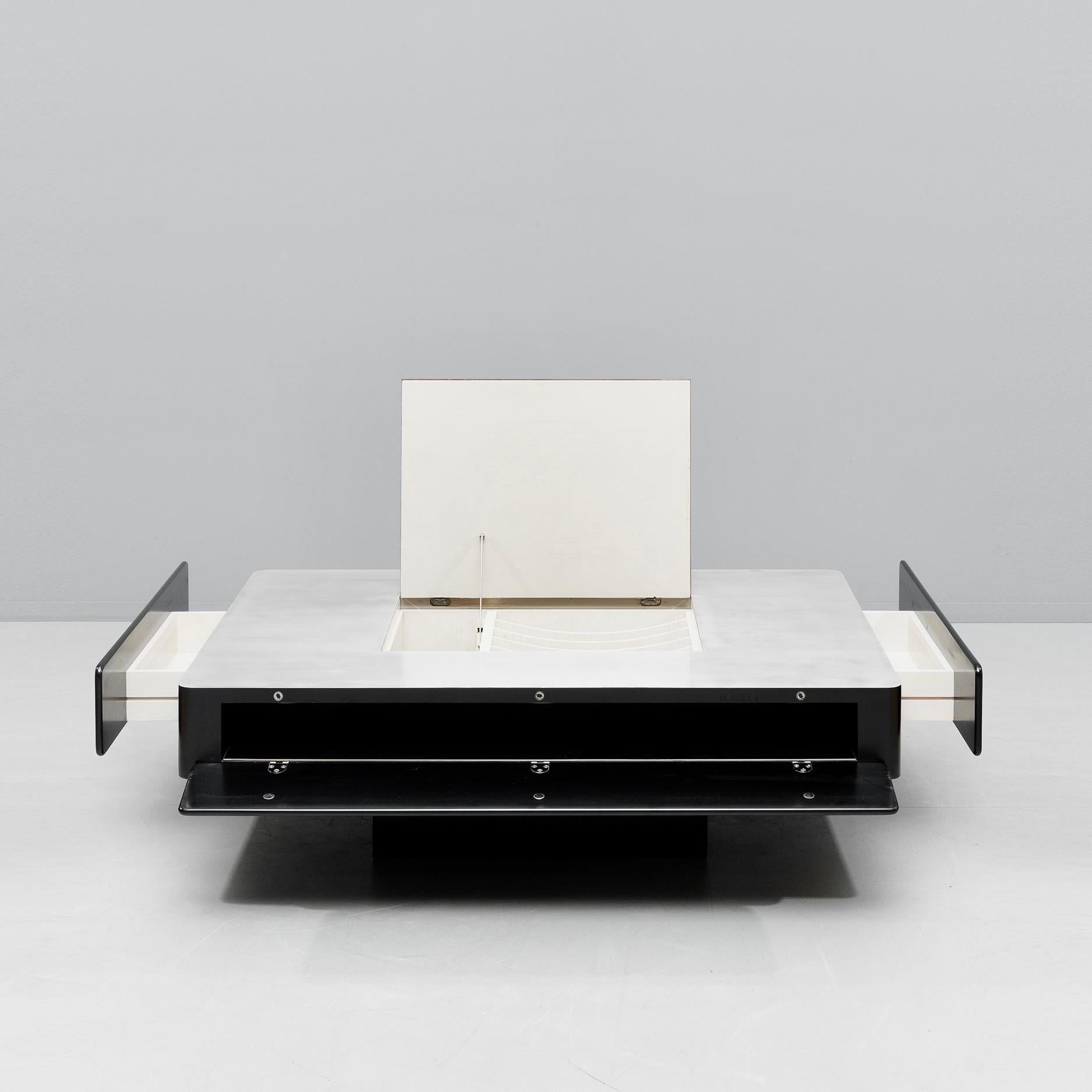 The table is made of black satin lacquered wood with a brushed stainless steel top. The top has a central door, opening to a compartment for music records, bottles, etc.  The door gently shuts with an adjustable damping system. There are two drawers