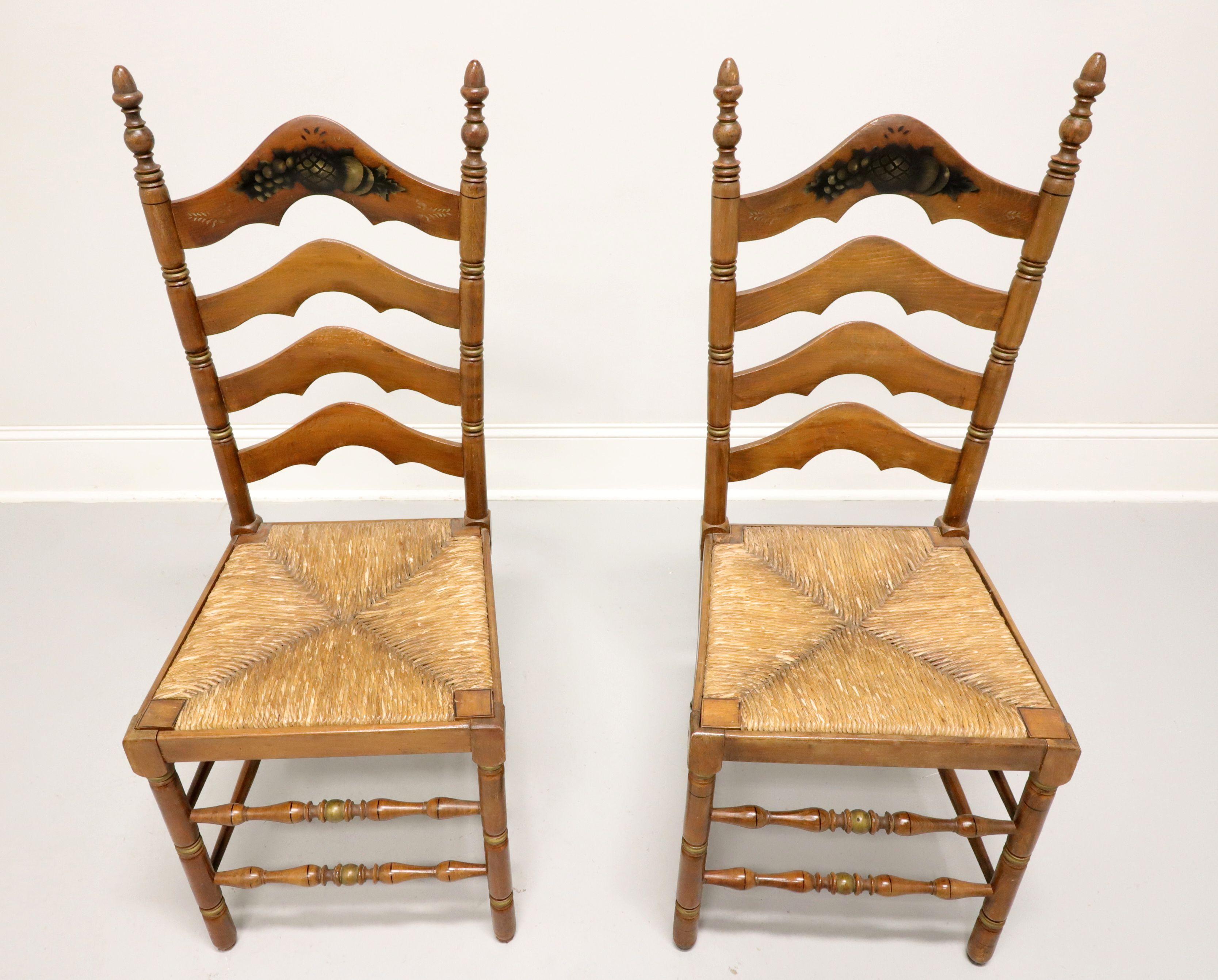 A pair of Cottage / Farmhouse style dining side chairs by Cape Ann Chairs. Maple with carved arched ladder back design, fruit stenciling to front of crest rail, finial capped stiles, rush seats, turned front legs & front stretchers, and solid back