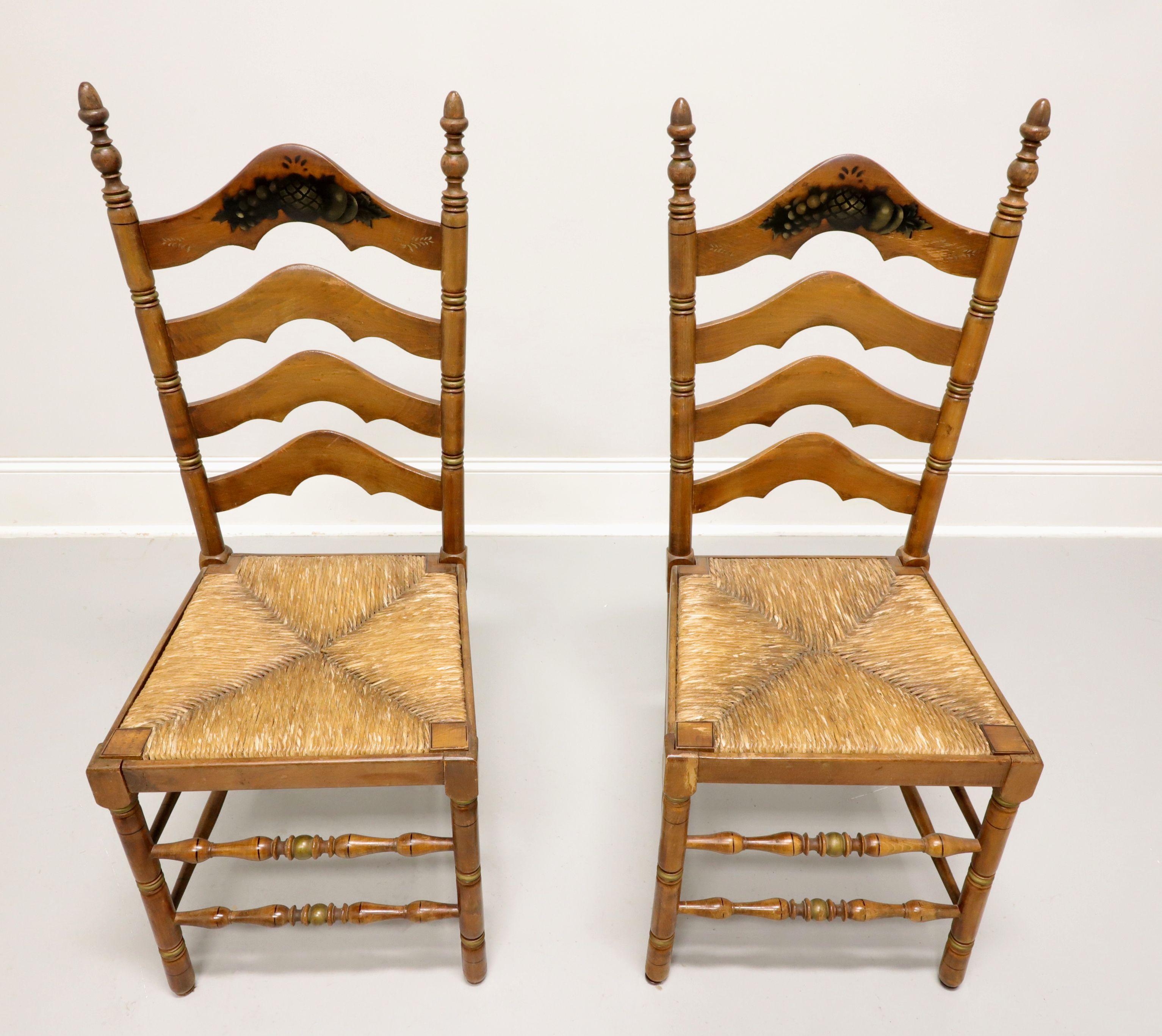 A pair of Cottage / Farmhouse style dining side chairs by Cape Ann Chairs. Maple with carved arched ladder back design, fruit stenciling to front of crest rail, finial capped stiles, rush seats, turned front legs & front stretchers, and solid back