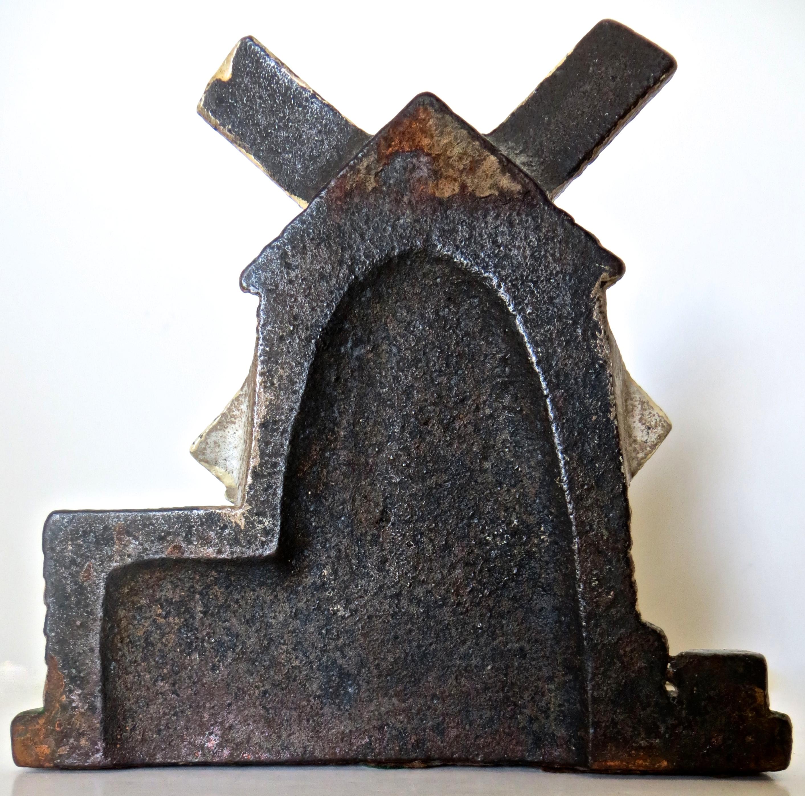 Cast iron doorstop depicts a windmill that perhaps exists in Cape Cod, with detailed casting of offset blades to the windmill itself, bricks to the facing of the housing structure, and steps leading up to both doorways. Manufactured by 