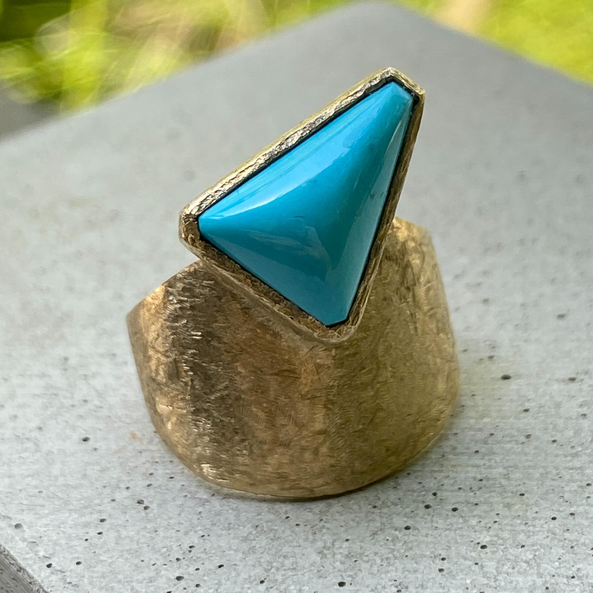 This abstract and unusual ring was designed, set and finished by Eytan Brandes.  It features a triangular cabochon of genuine Sleeping Beauty Turquoise on a bezel platform rising from a gorgeous tapered band in 14K yellow gold.  The band has a